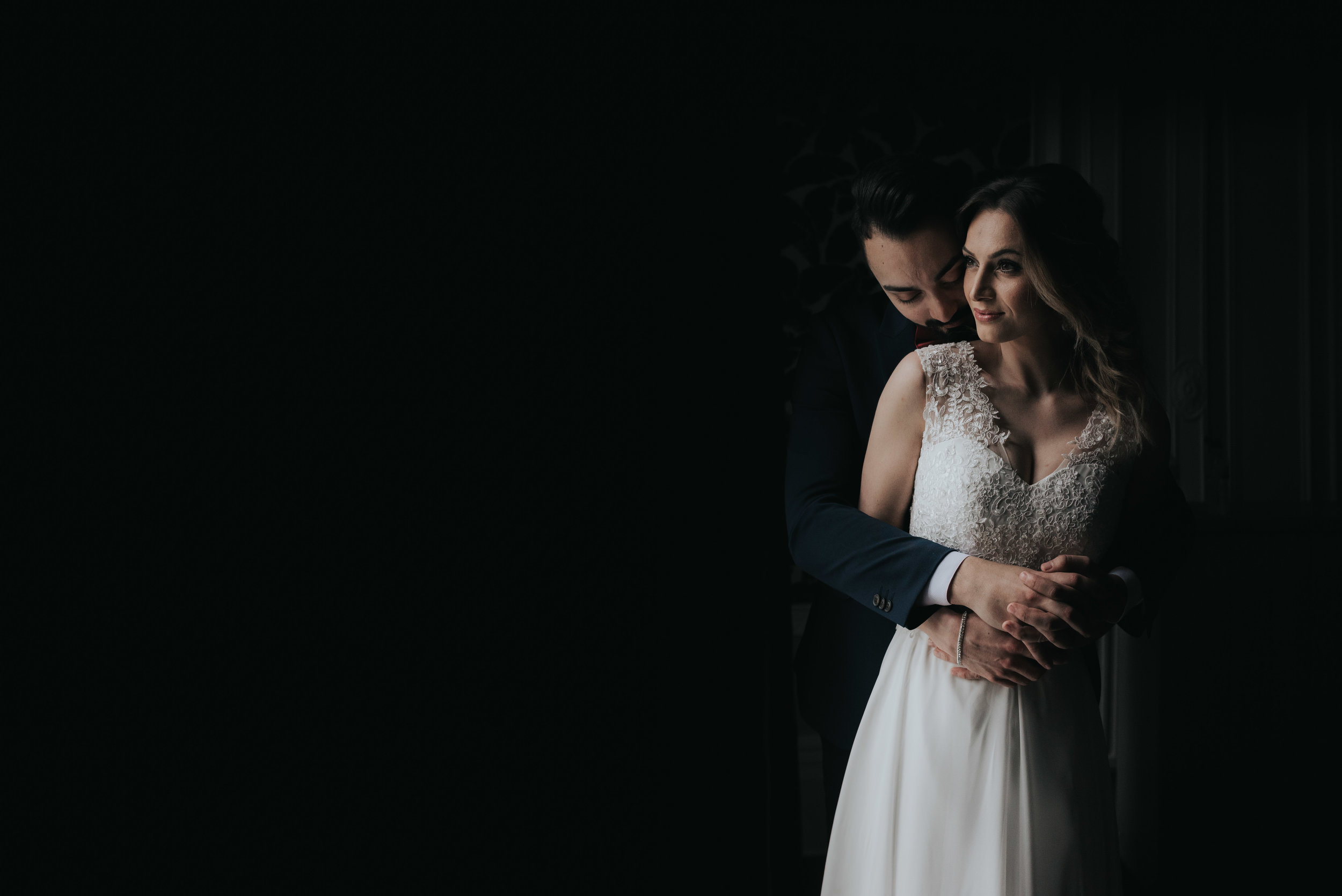 bride and groom stand by the window with the light shining on the right side of them