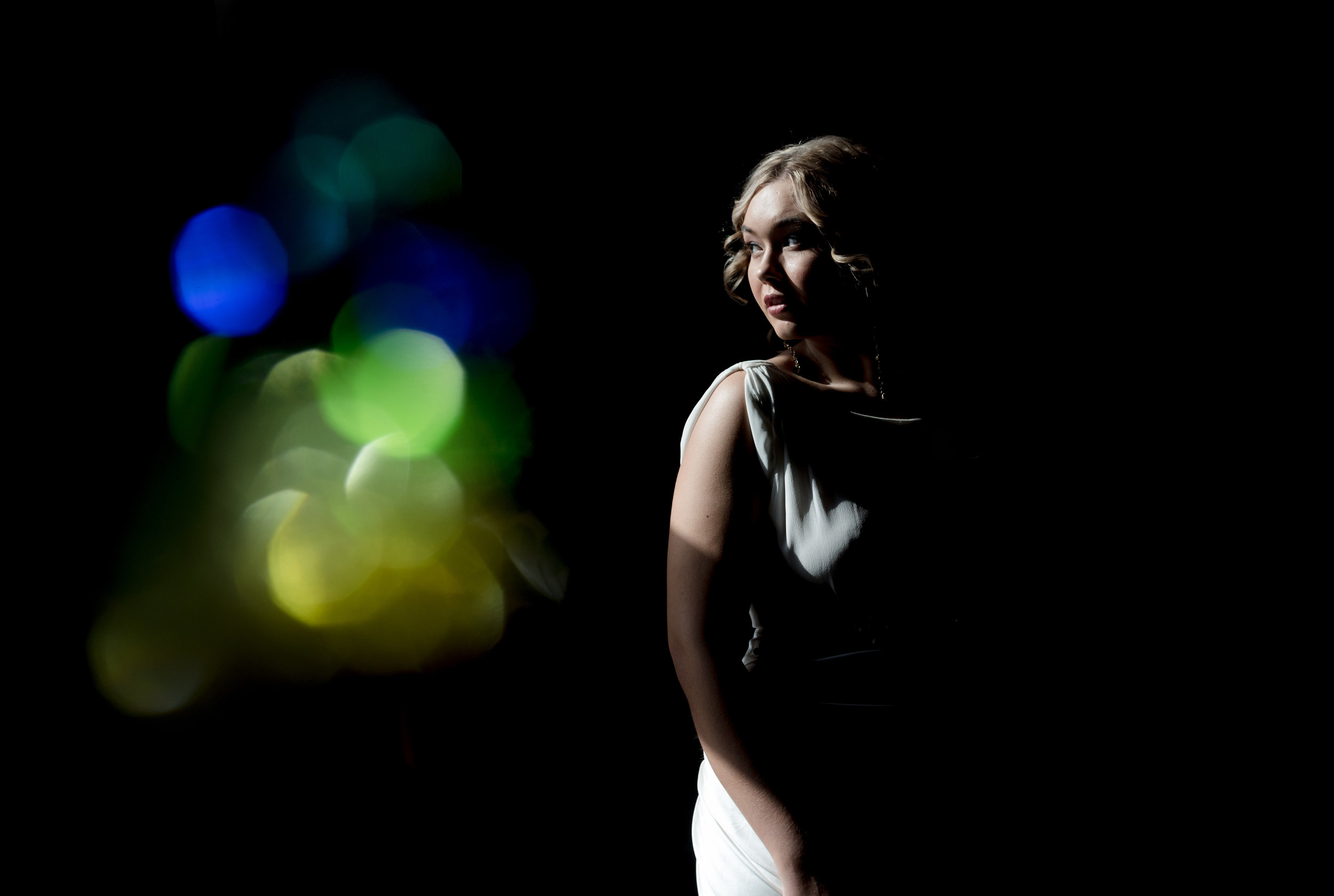 the bride stands in the window while light from the sun reflects through a prism, casting colour in the image