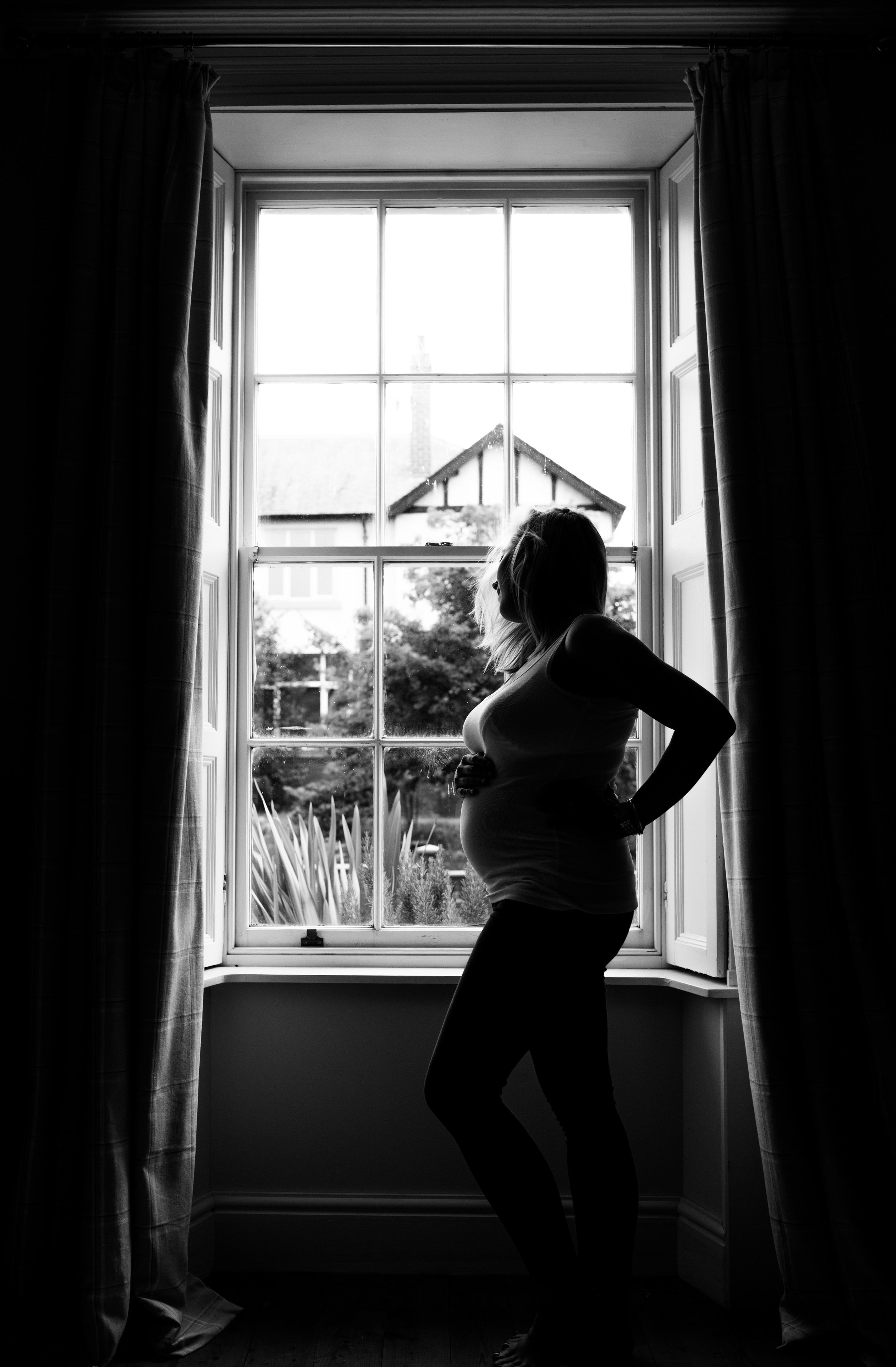 Pregnant lady stands against the window of her Carlisle home for her maternity photo shoot.