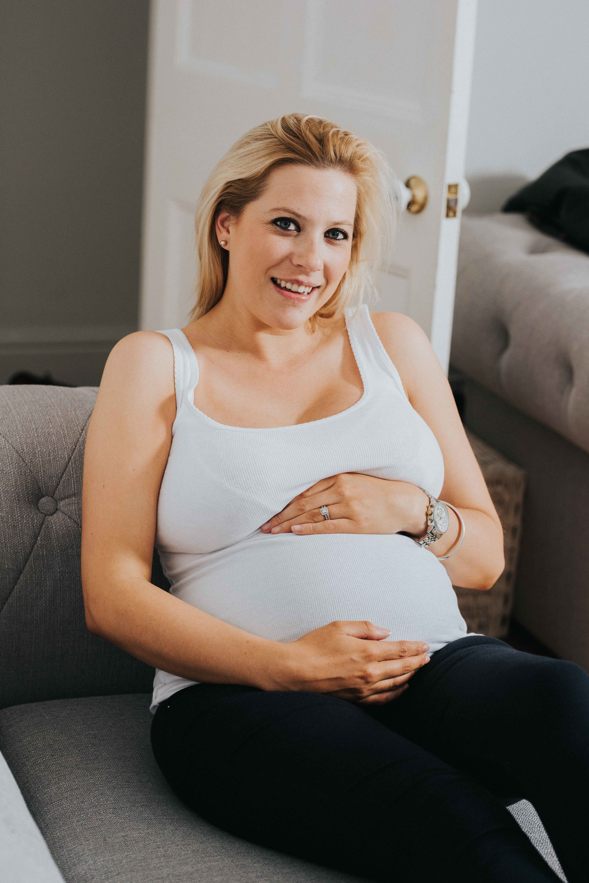 Pregnant Chloe faces the camera whilst sitting on her sofa relaxing.