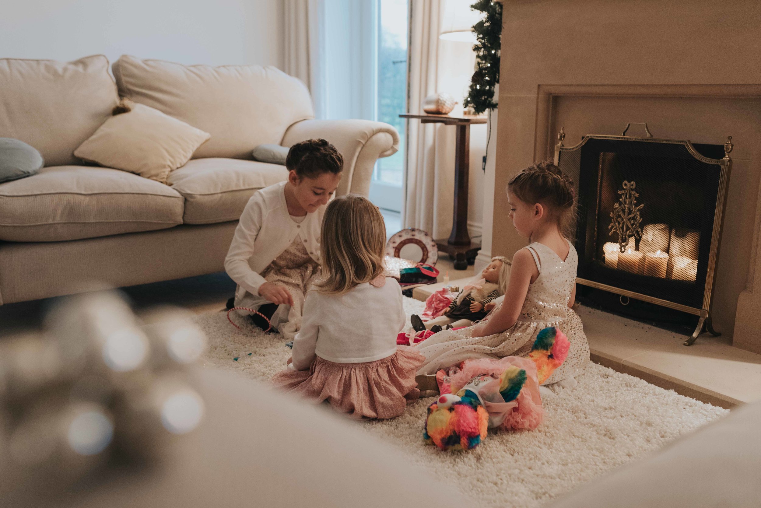 Three children sit together on a rug in front of the fireplace during Christening celebrations.