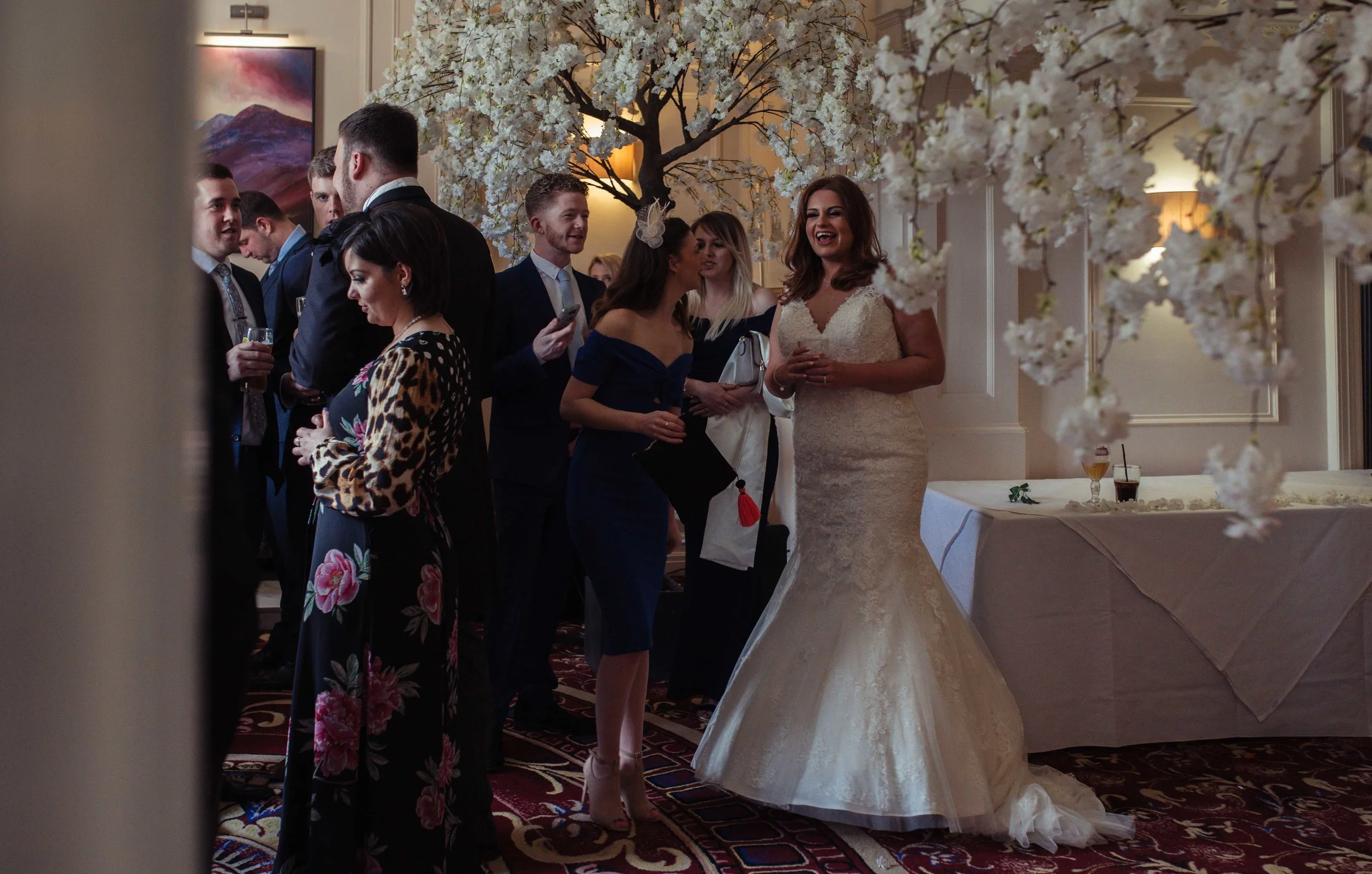 the bride stands in the wedding reception venue and shares a smile and a laugh with some of her wedding guests