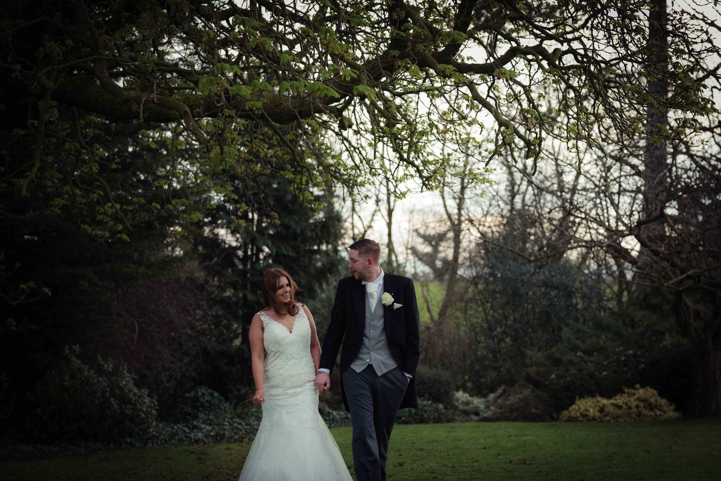 the bride and groom walk through the gardens of Crabwall Manor holding hands and chatting to each other