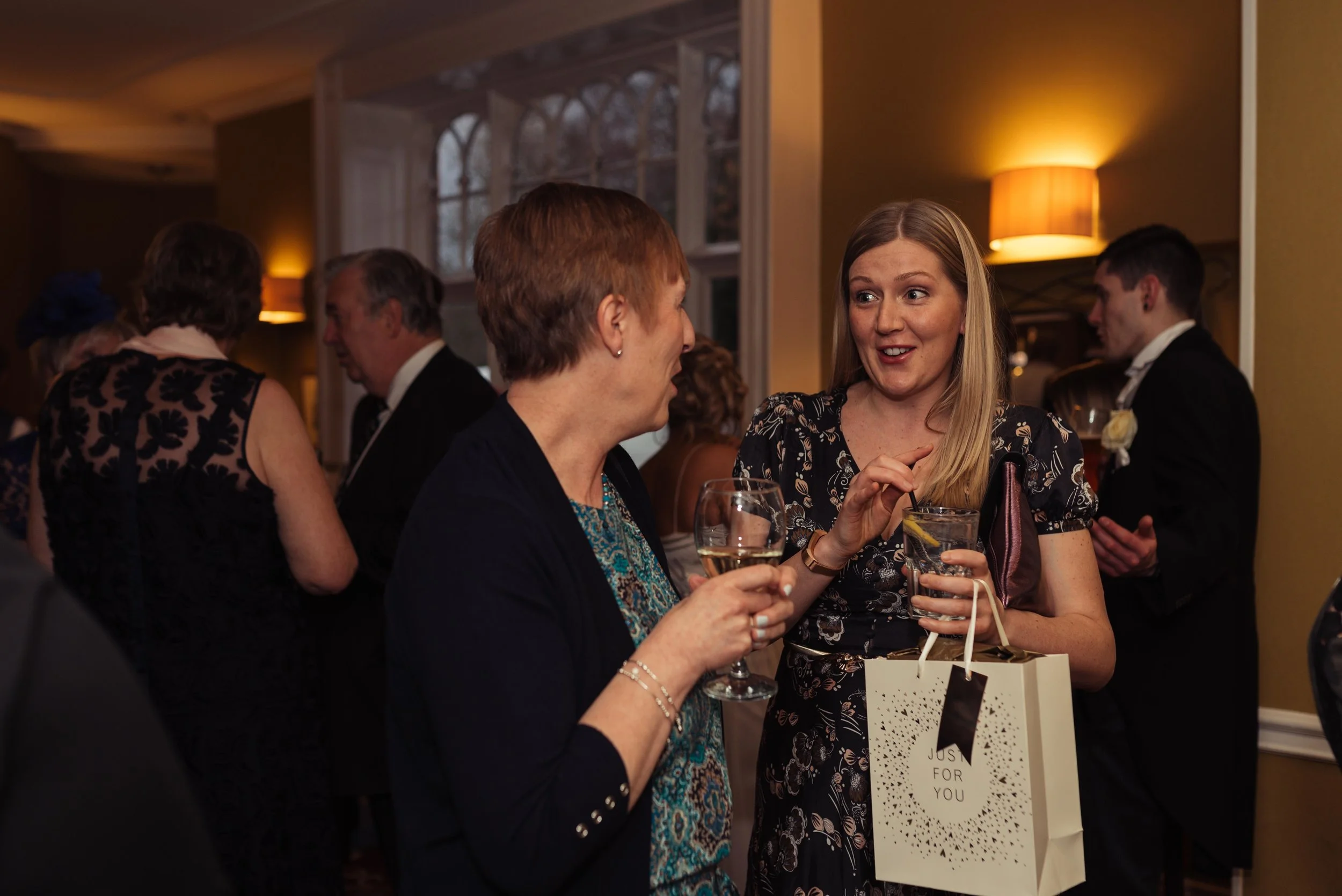 a wedding guest has a surprised look on her face talking to another of the guests