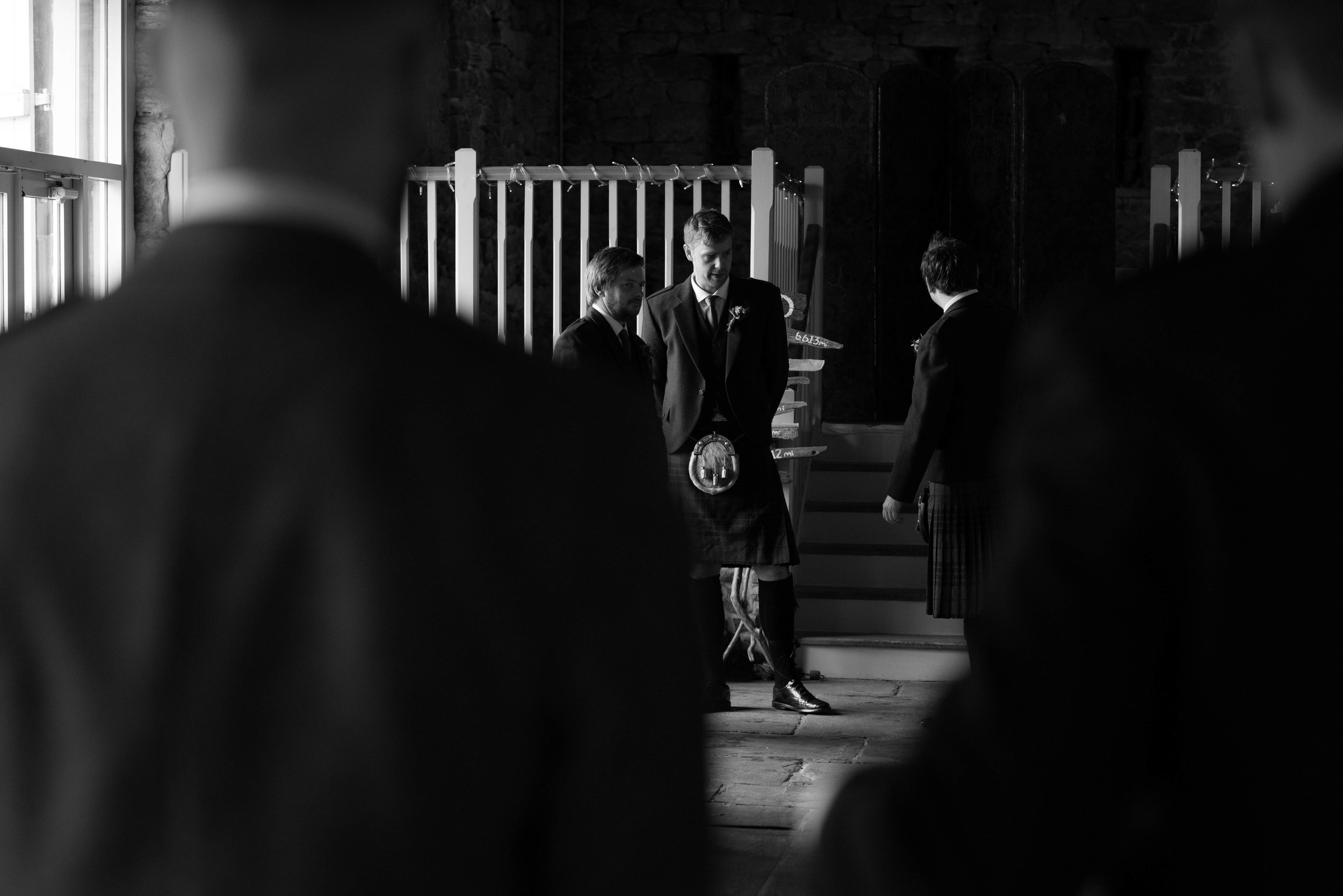Groomsmen stand at the back of Askham Hall barn to direct wedding guests to their chairs
