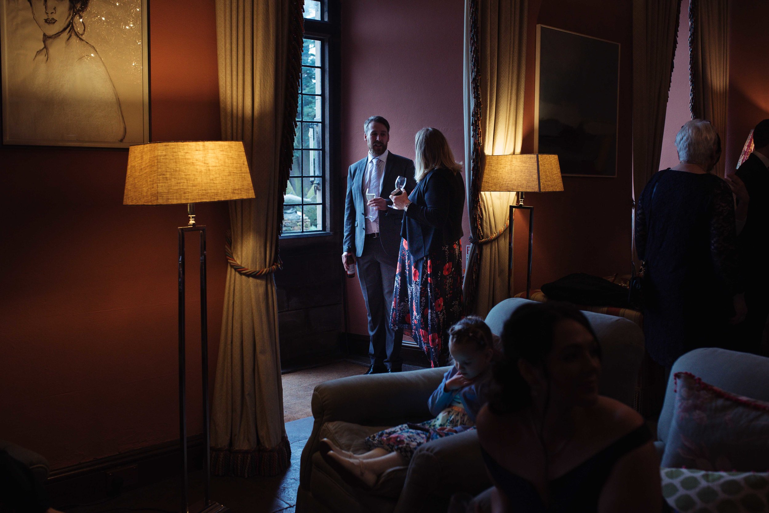 Two wedding guests stand in the doorway, they are lit with daylight coming in through the window