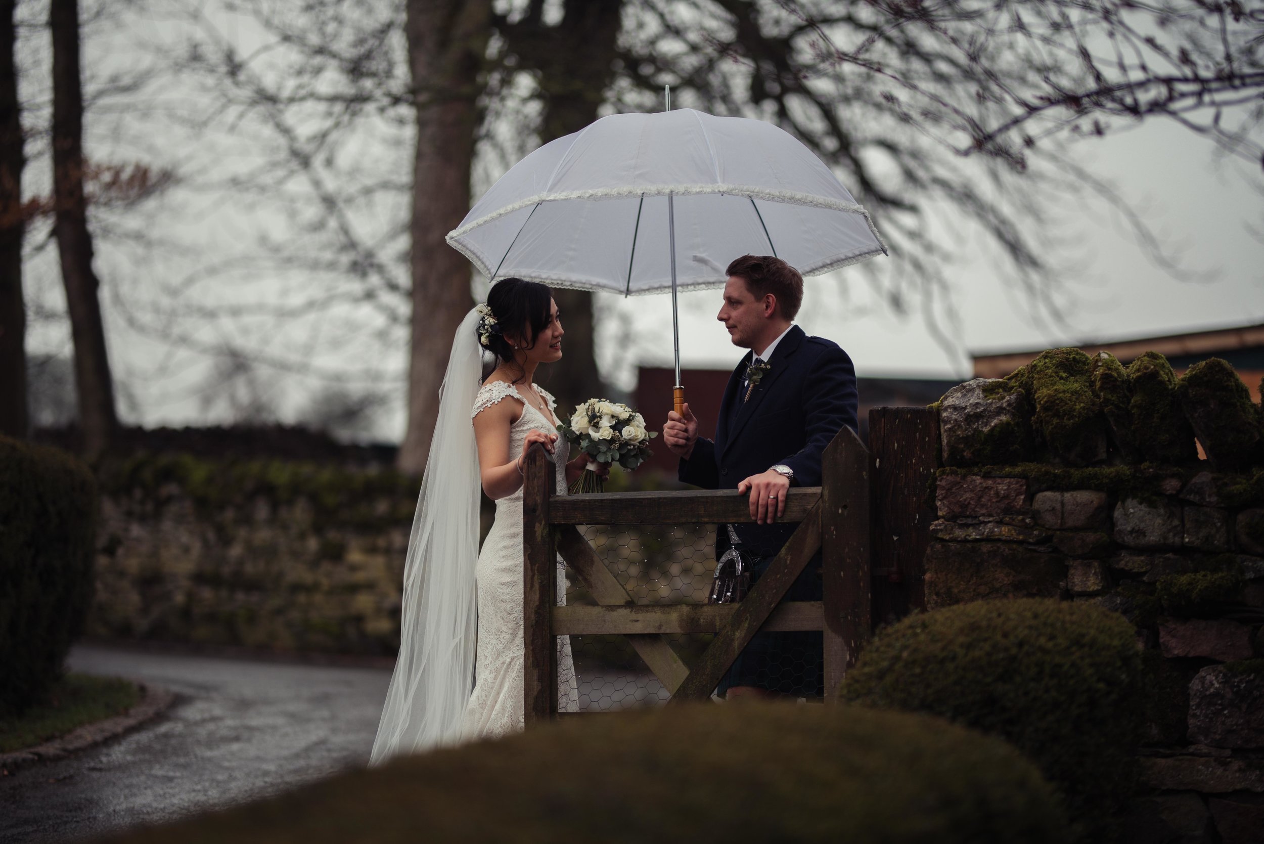 The bride and groom stand under a white umbrella for their wedding photography at Askham Hall