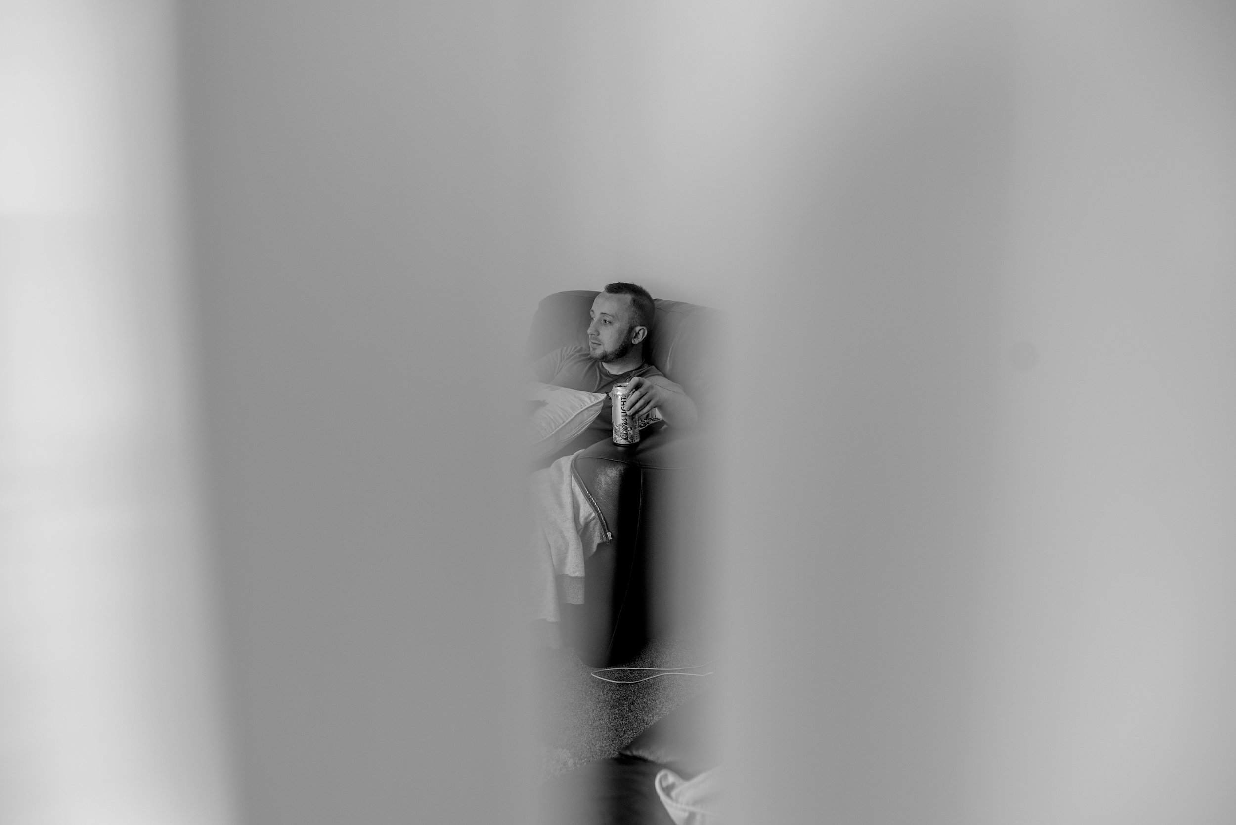 Groomsman sitting on a chair with a can of foster, taken through a crack in the door.