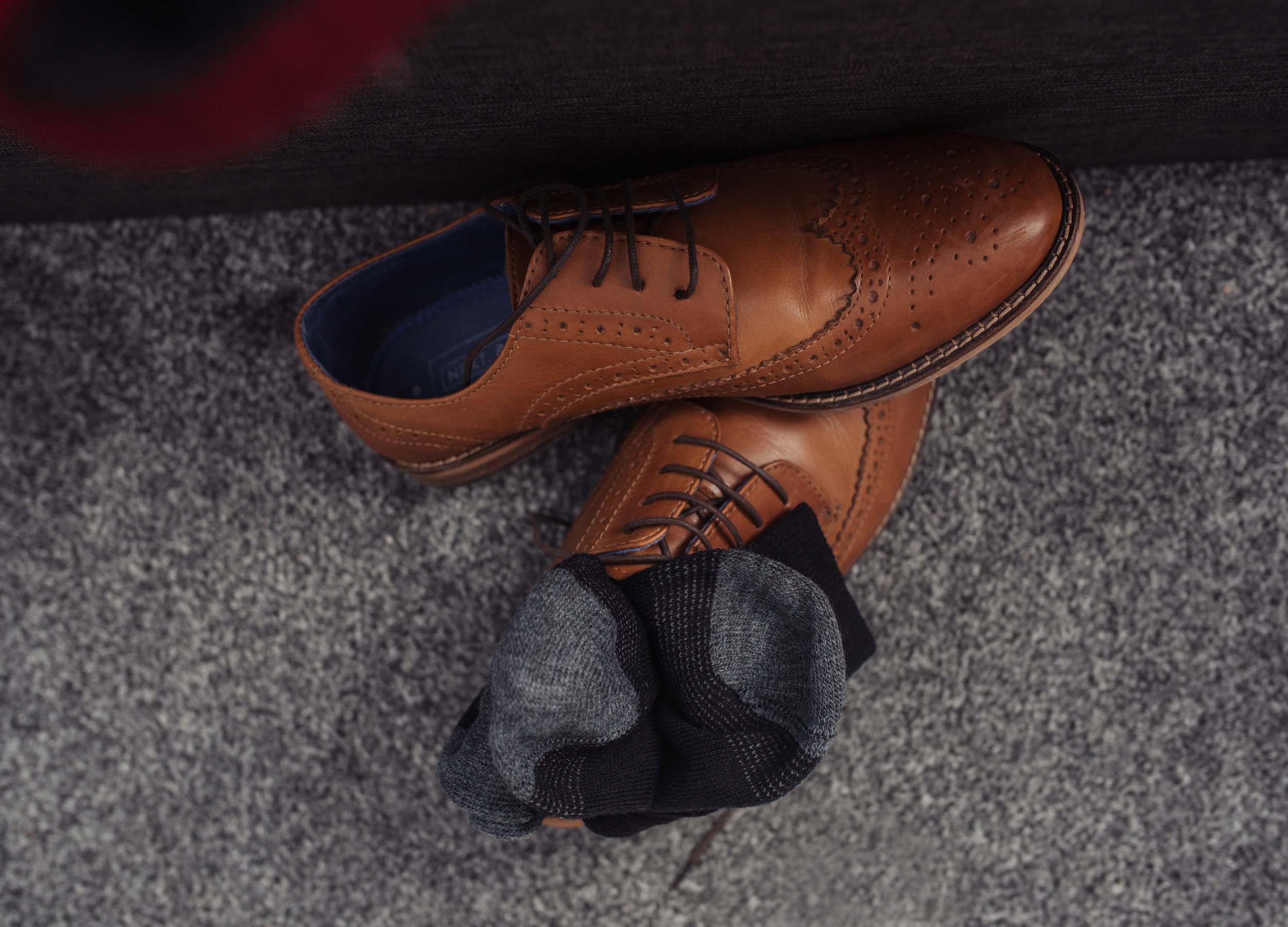 The grooms brown brogues lie on the floor with his socks on top of the shoes.