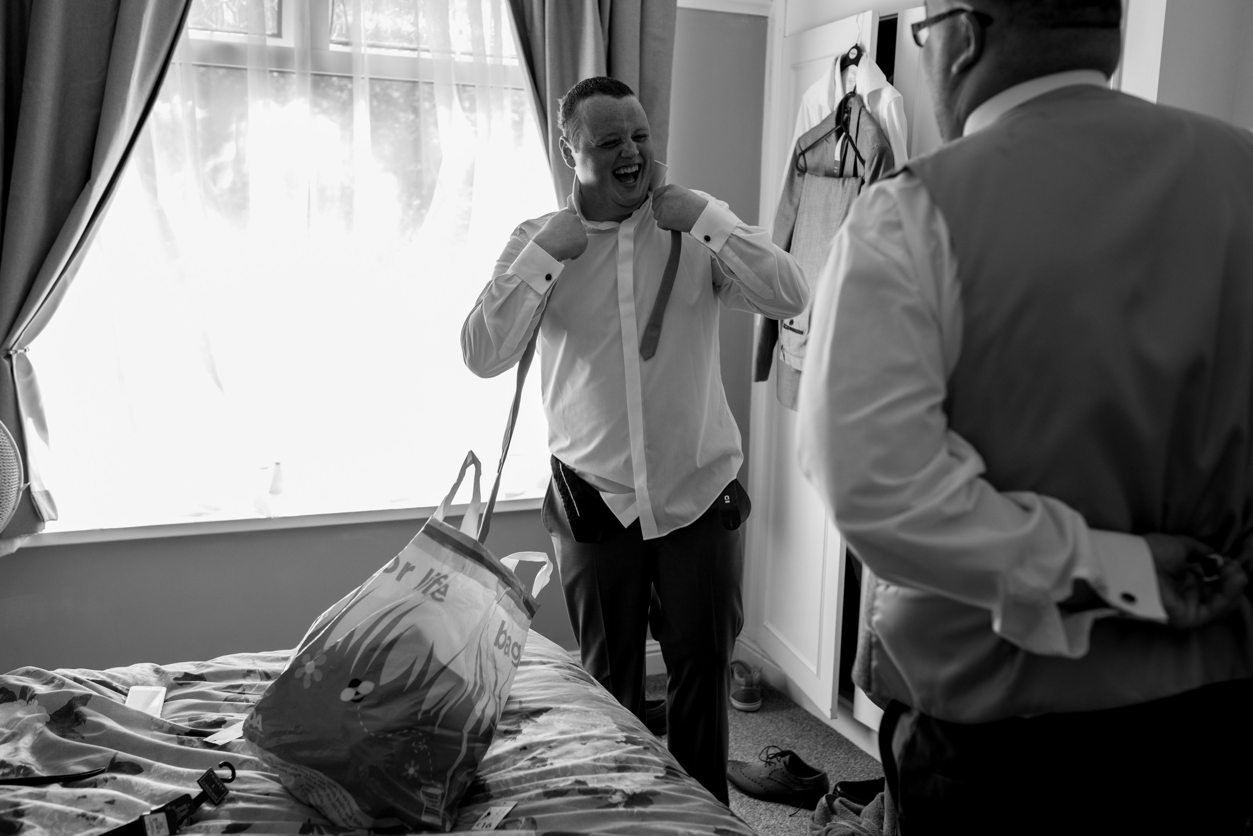 Groom ties his tie while laughing towards the best man.