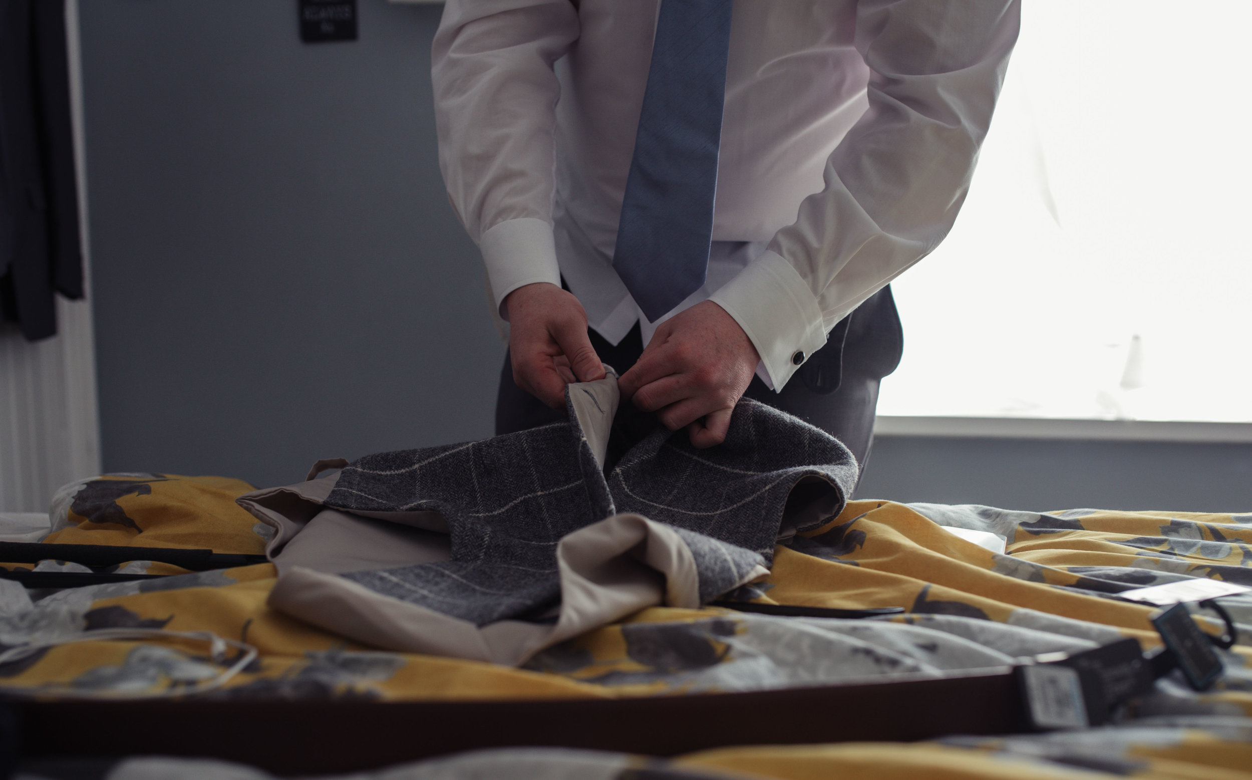 The groom leans over the bed to unbutton his waistcoat