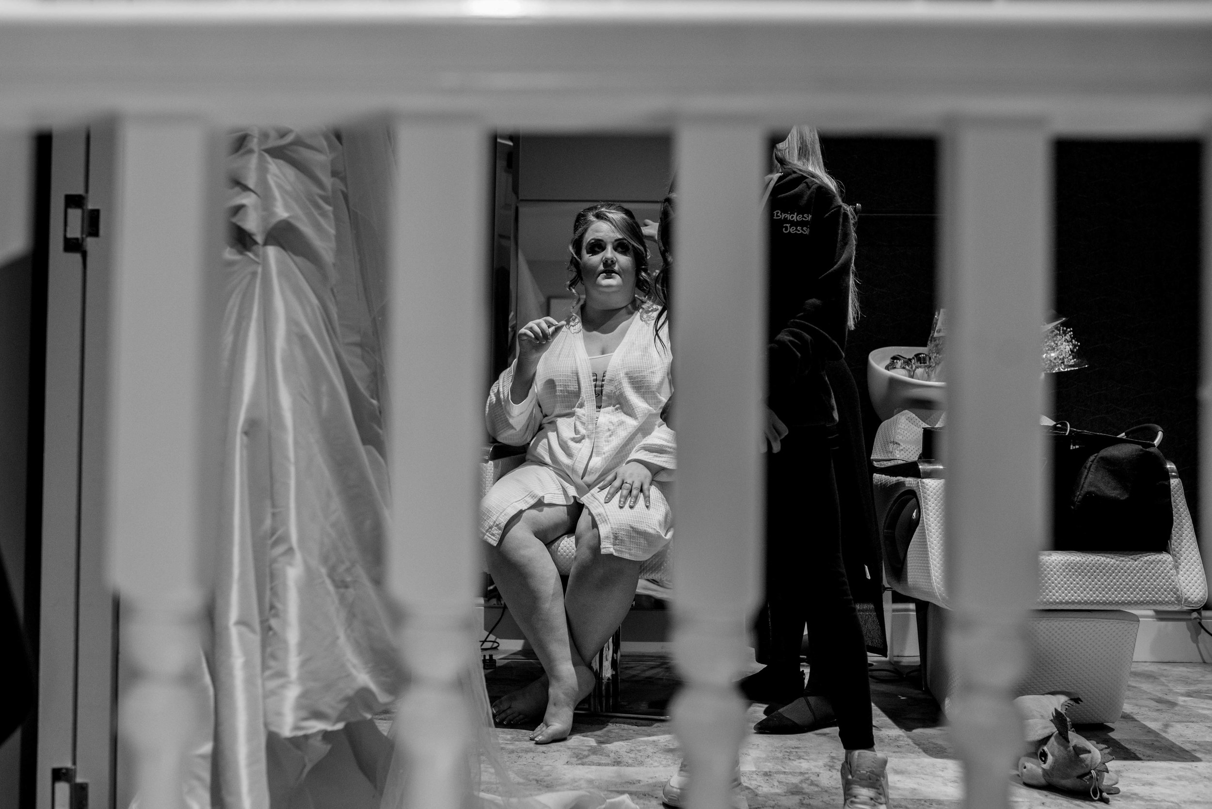 The bride is seen through gaps in the bannister rail while she gets ready for her wedding.