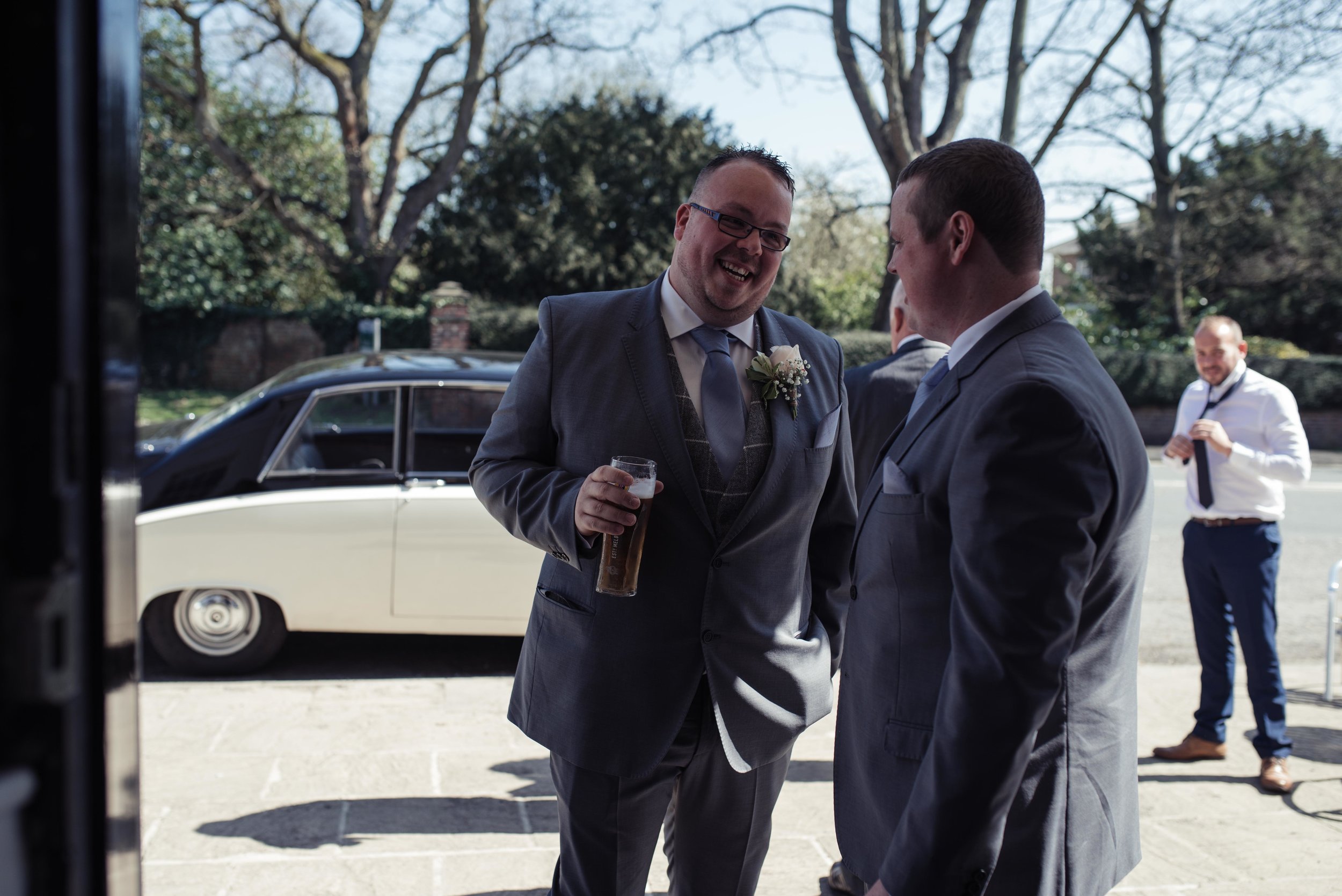 The groom and best man stand outside the wedding venue while the guests arrive.