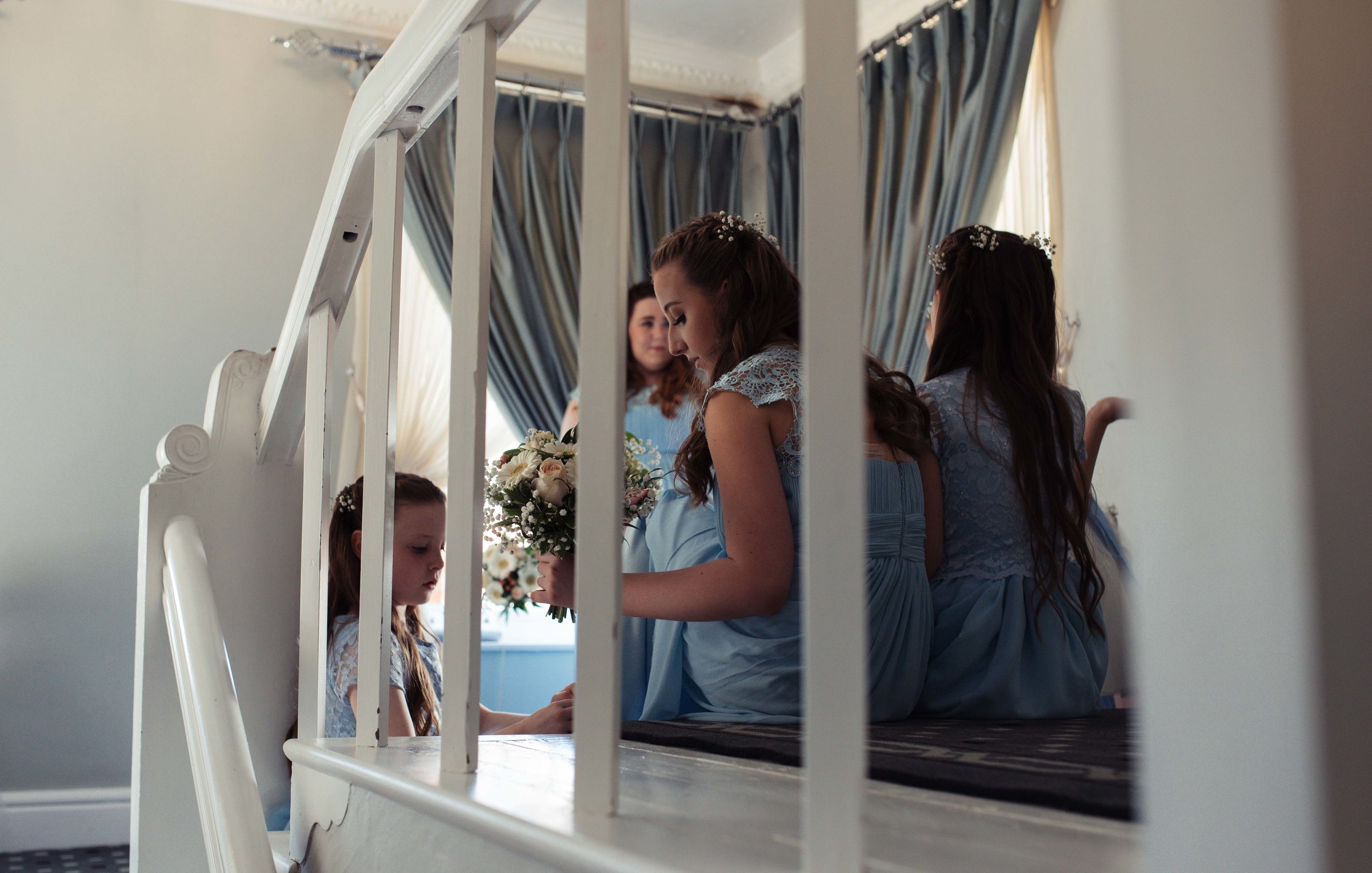 Flower girls and bridesmaids sit on the stairs of the wedding venue and wait for the bride to appear.