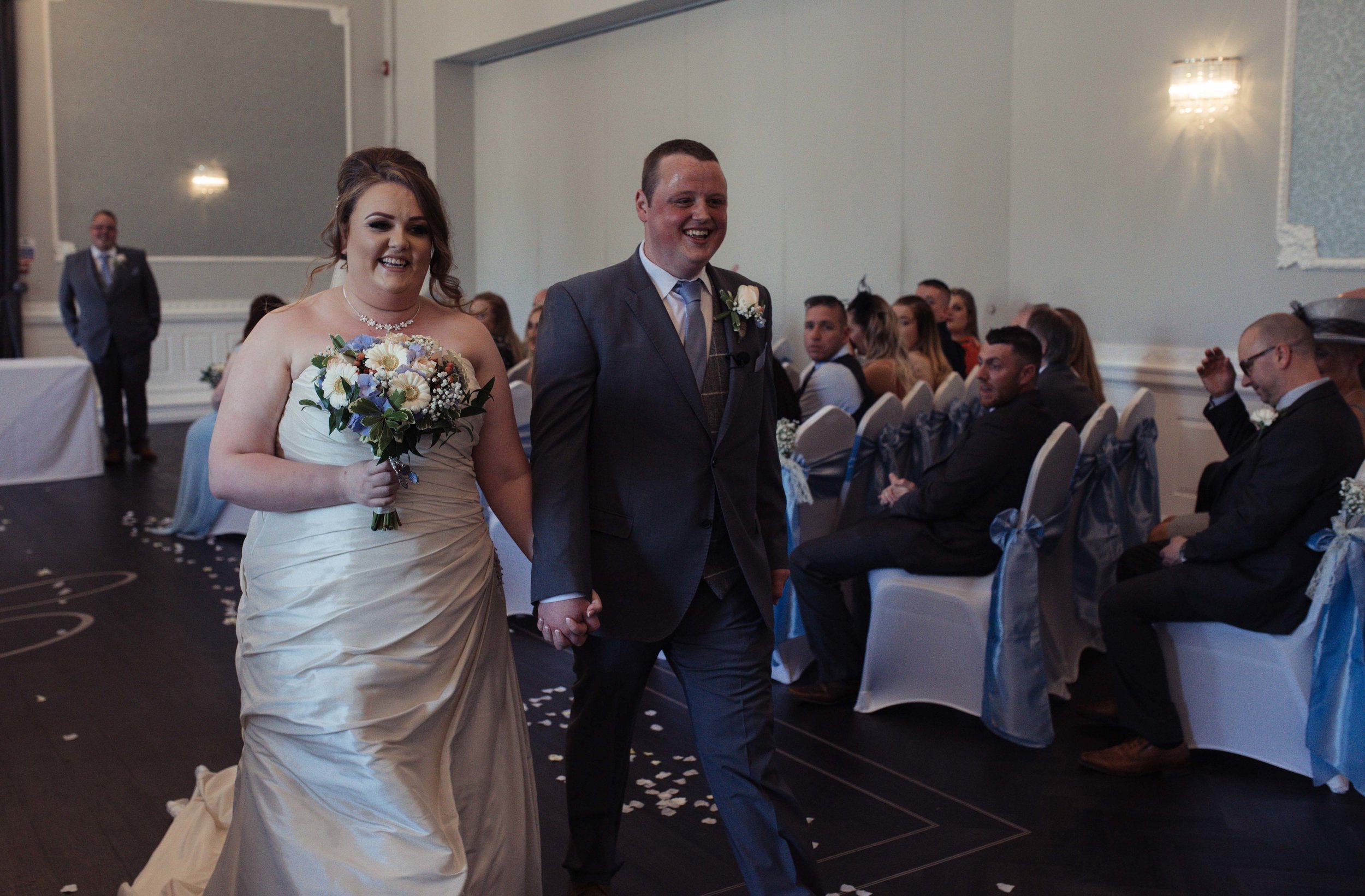 Smiling bride and groom walk out of the ceremony venue together, holding hands