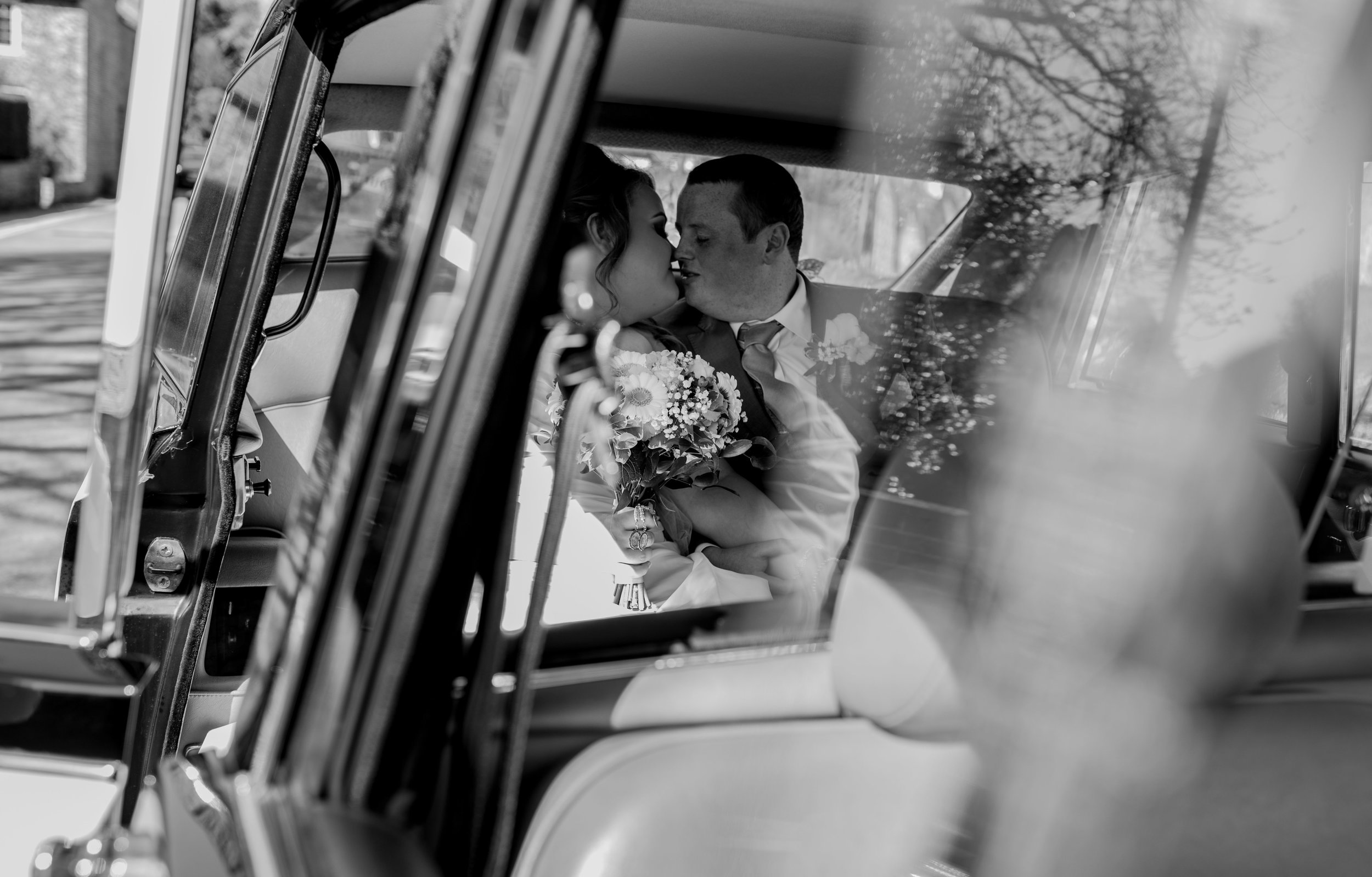 Bride and groom share a kiss in the back of the wedding car