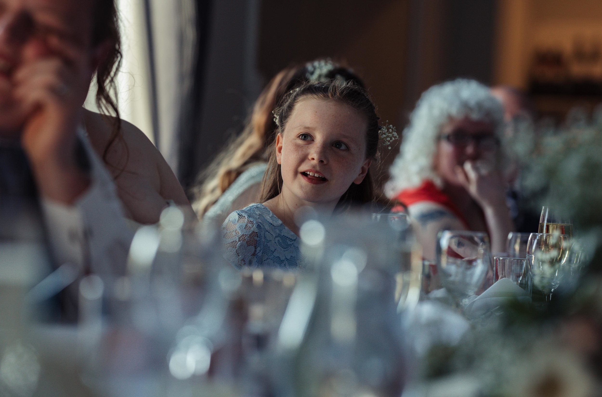 The bride and grooms daughter has a smile while she is being talked about during the wedding speeches 