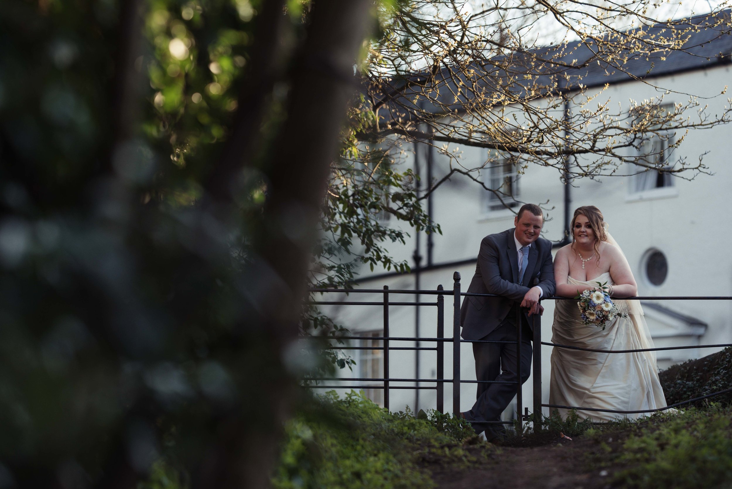 The bride and groom lean on a fence during their wedding photography 