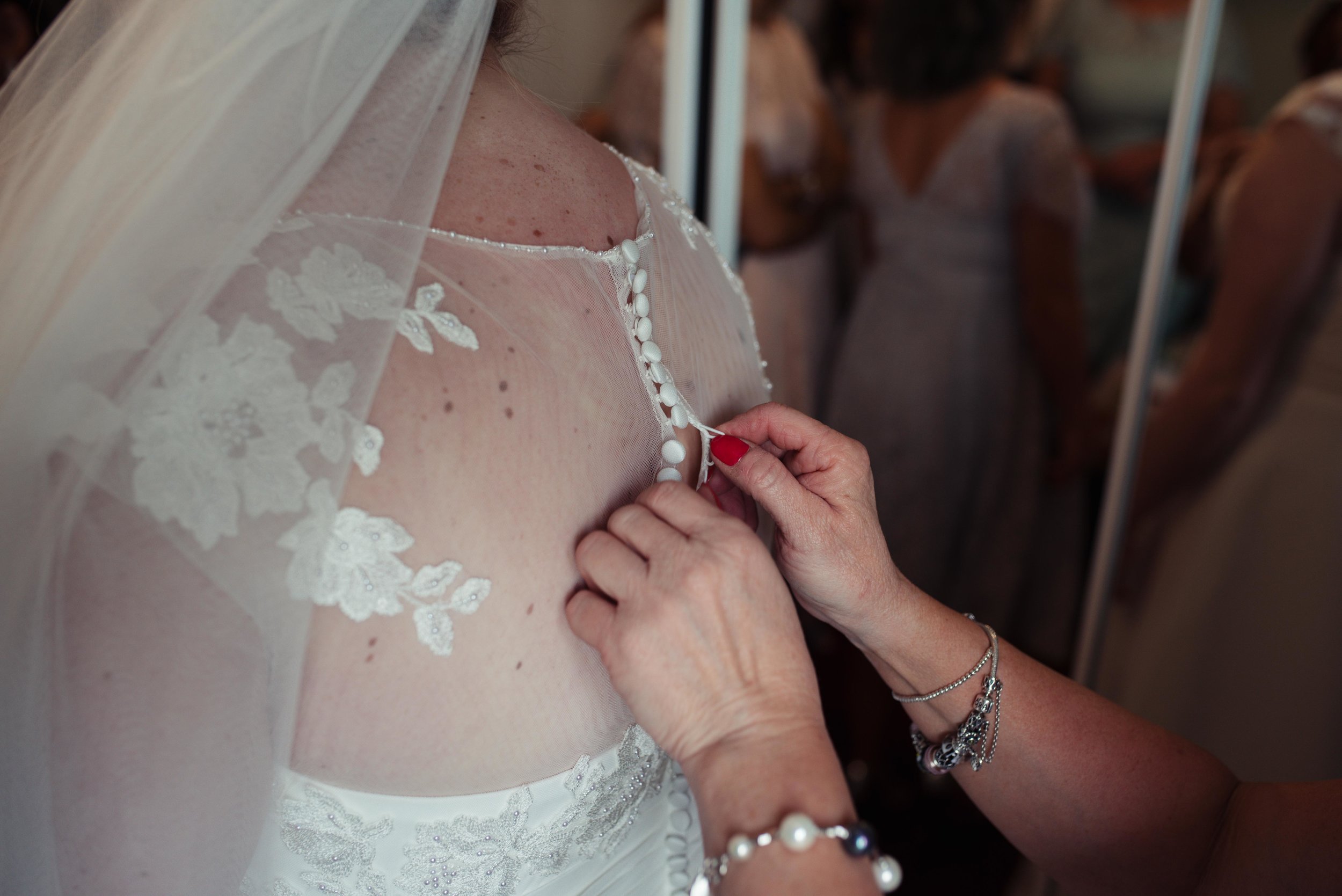 The bride is getting her dress buttoned up by her mother