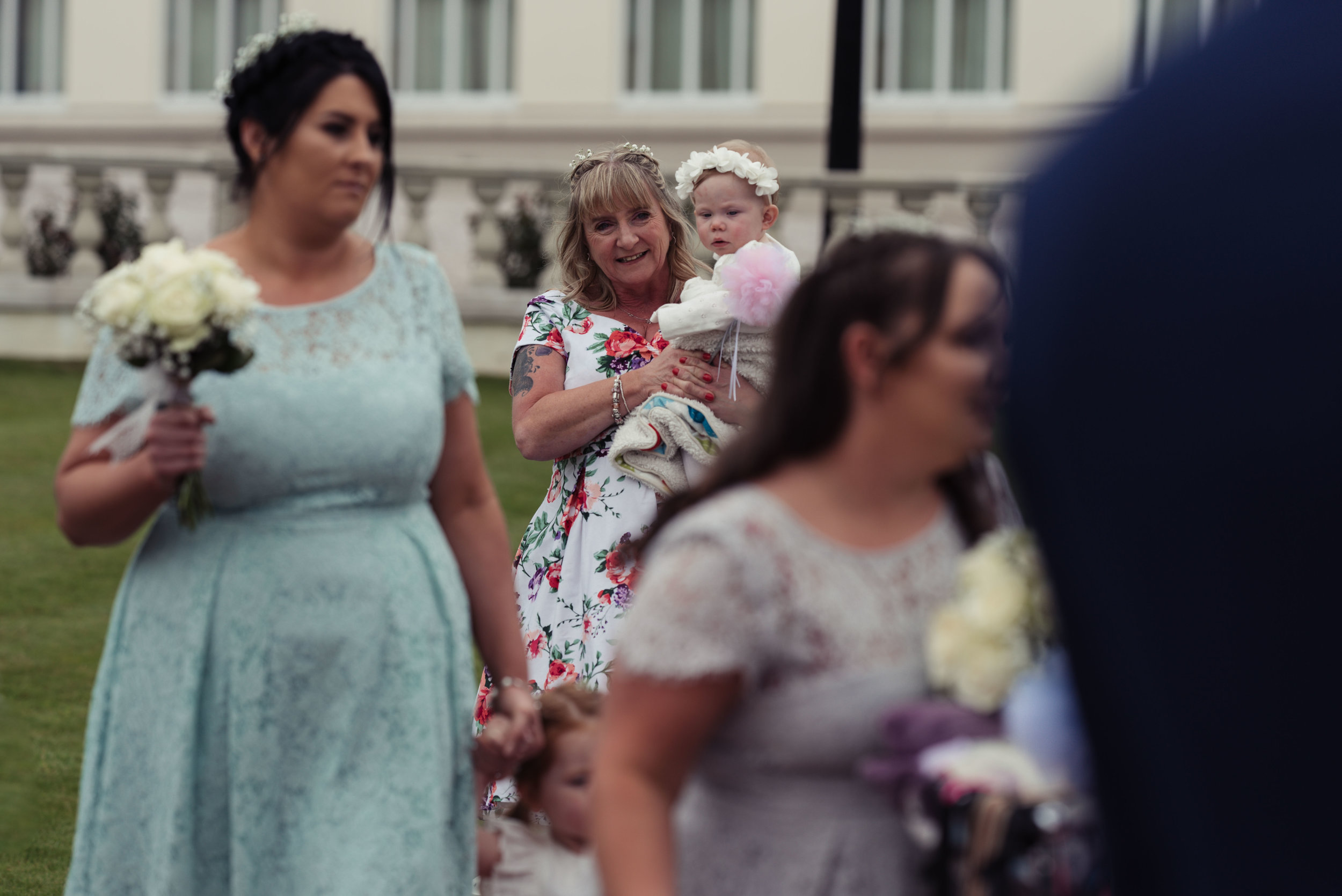 The brides mother carries a young flower girl up the aisle