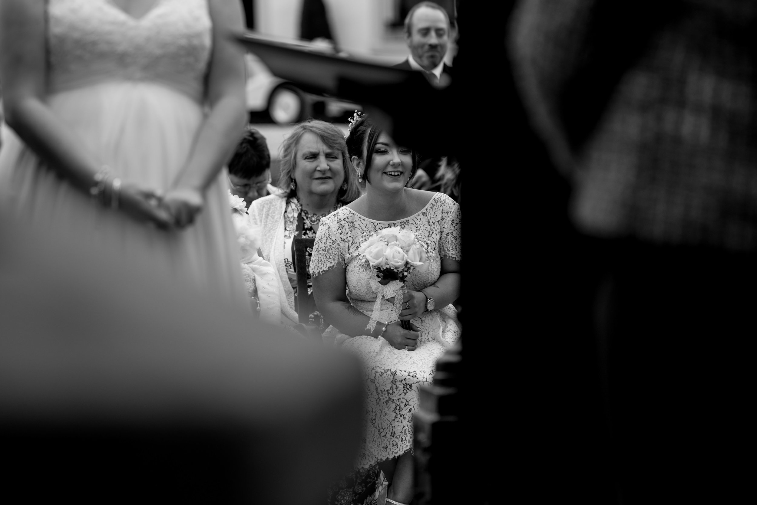 A bridesmaid sits smiling as the bride and groom exchange their vows