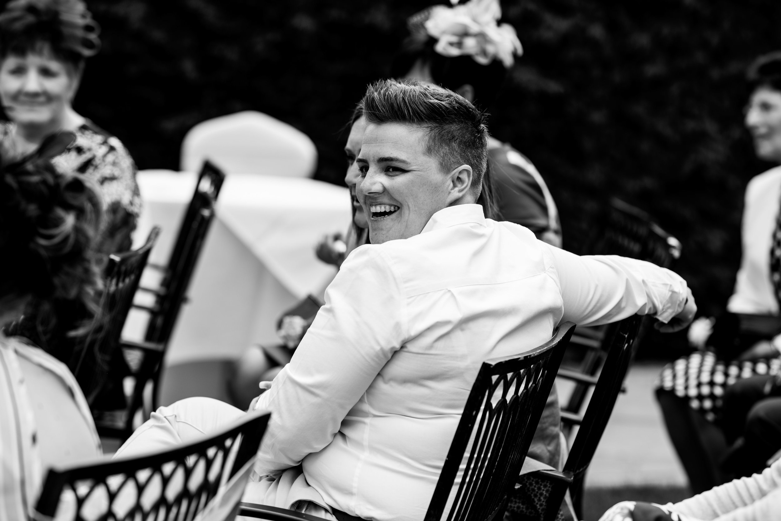 A wedding guest smiles at another guest across the garden at the end of the wedding cermony