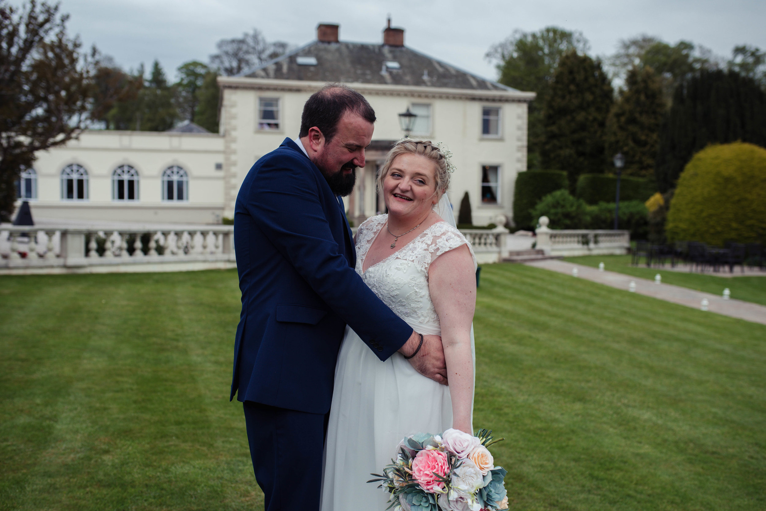 The bride and groom stand to have their photo taken outside the roundthorn country house
