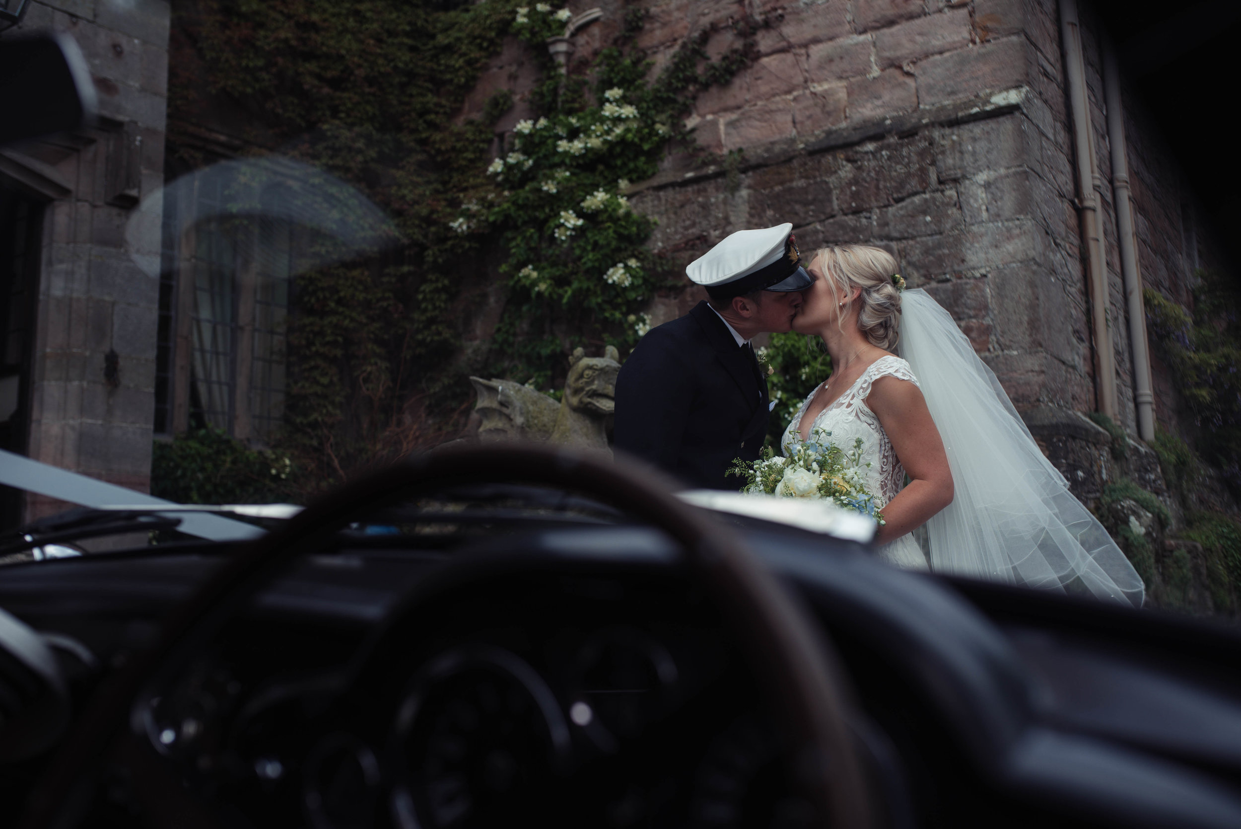 An aston martin provides the window through which the bride and groom can be seen kissing at askham hall