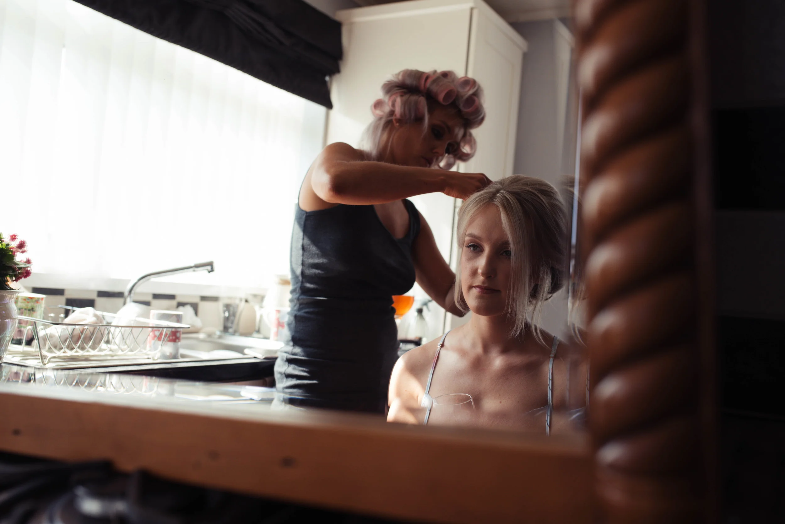 the bride looks into the mirror as she has her hair finished