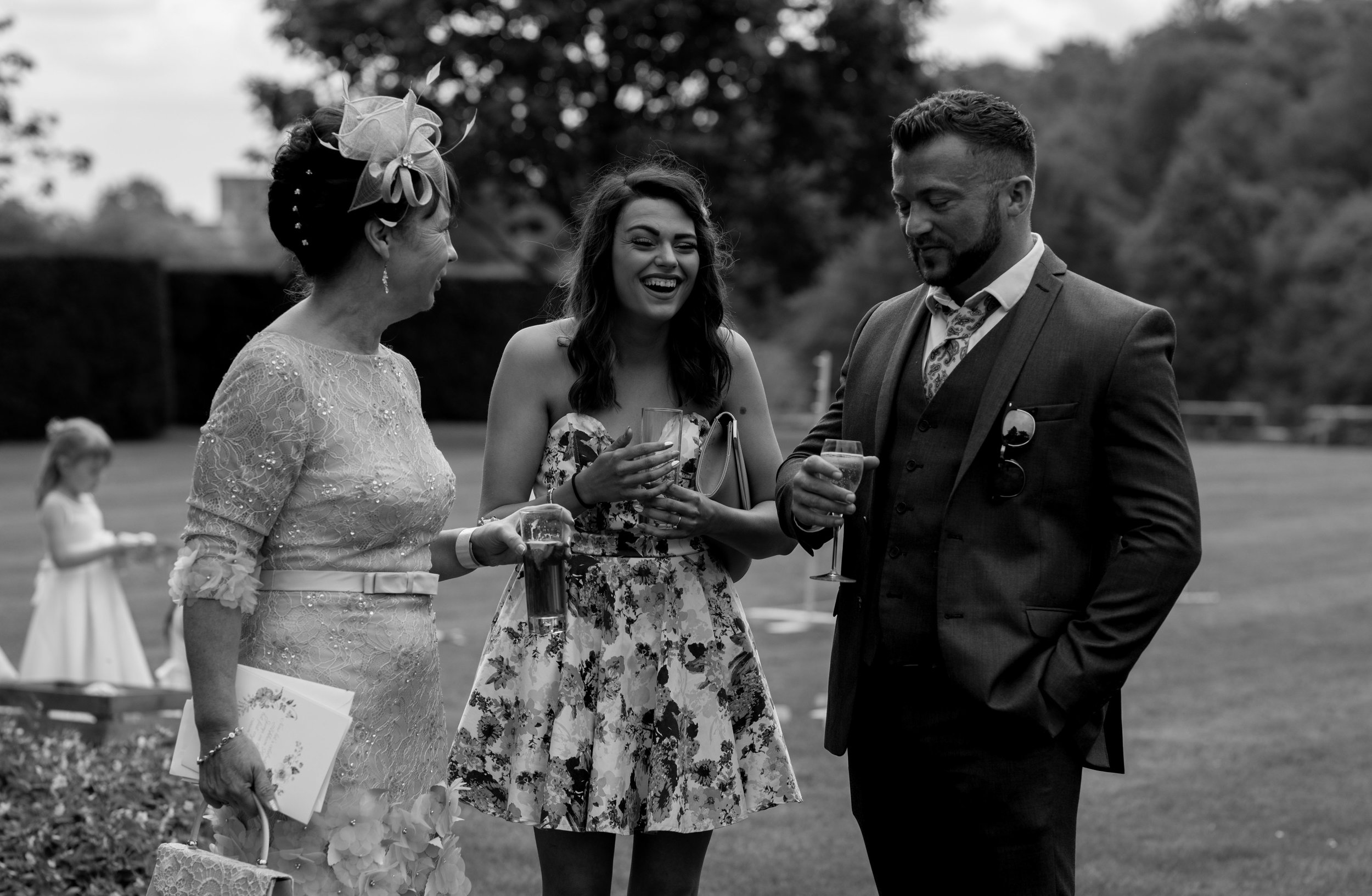 a girl in a short flowery dress laughs at a joke by one of the other wedding guests
