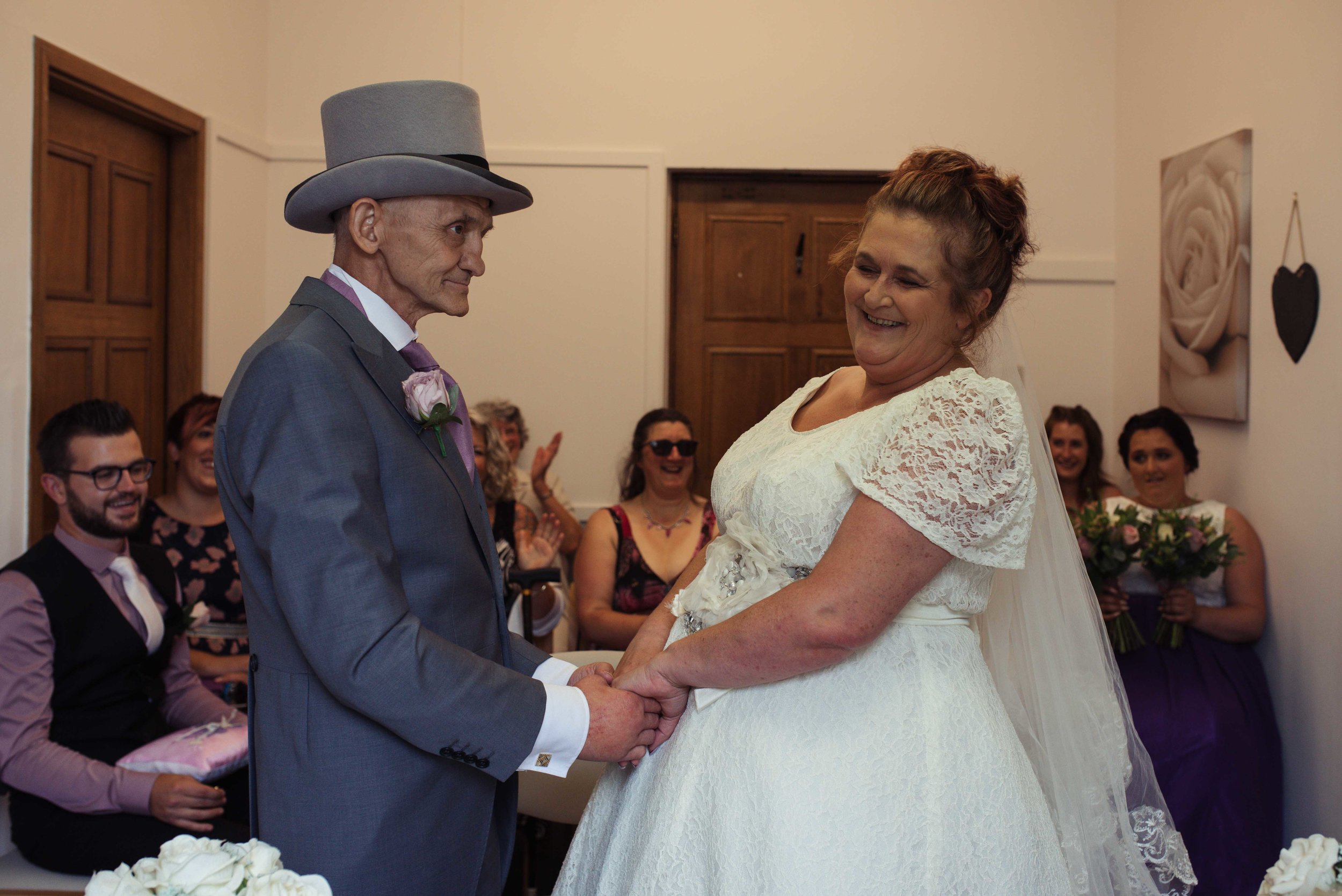 The groom makes the bride laugh as they stand holding hands during the wedding ceremony