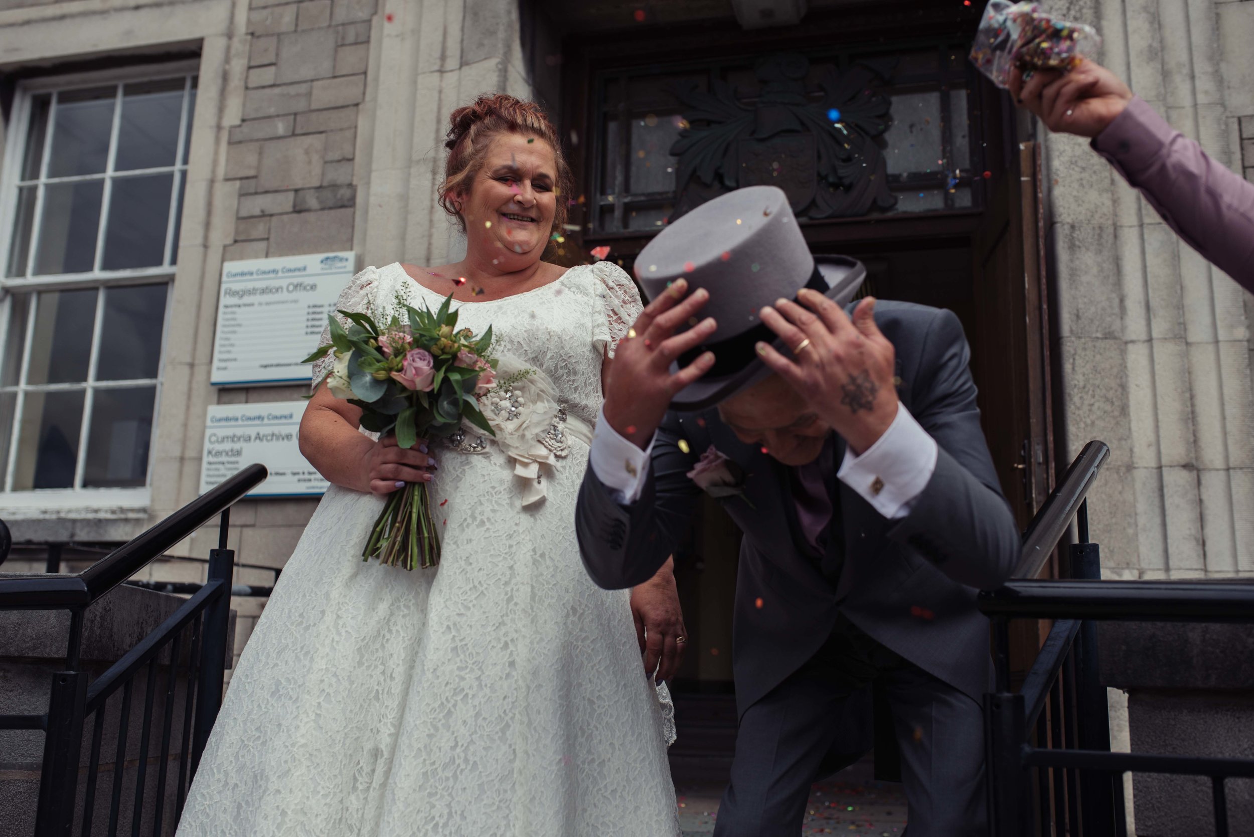 Confetti almost knocks the grooms hat off outside the cumbria wedding venue