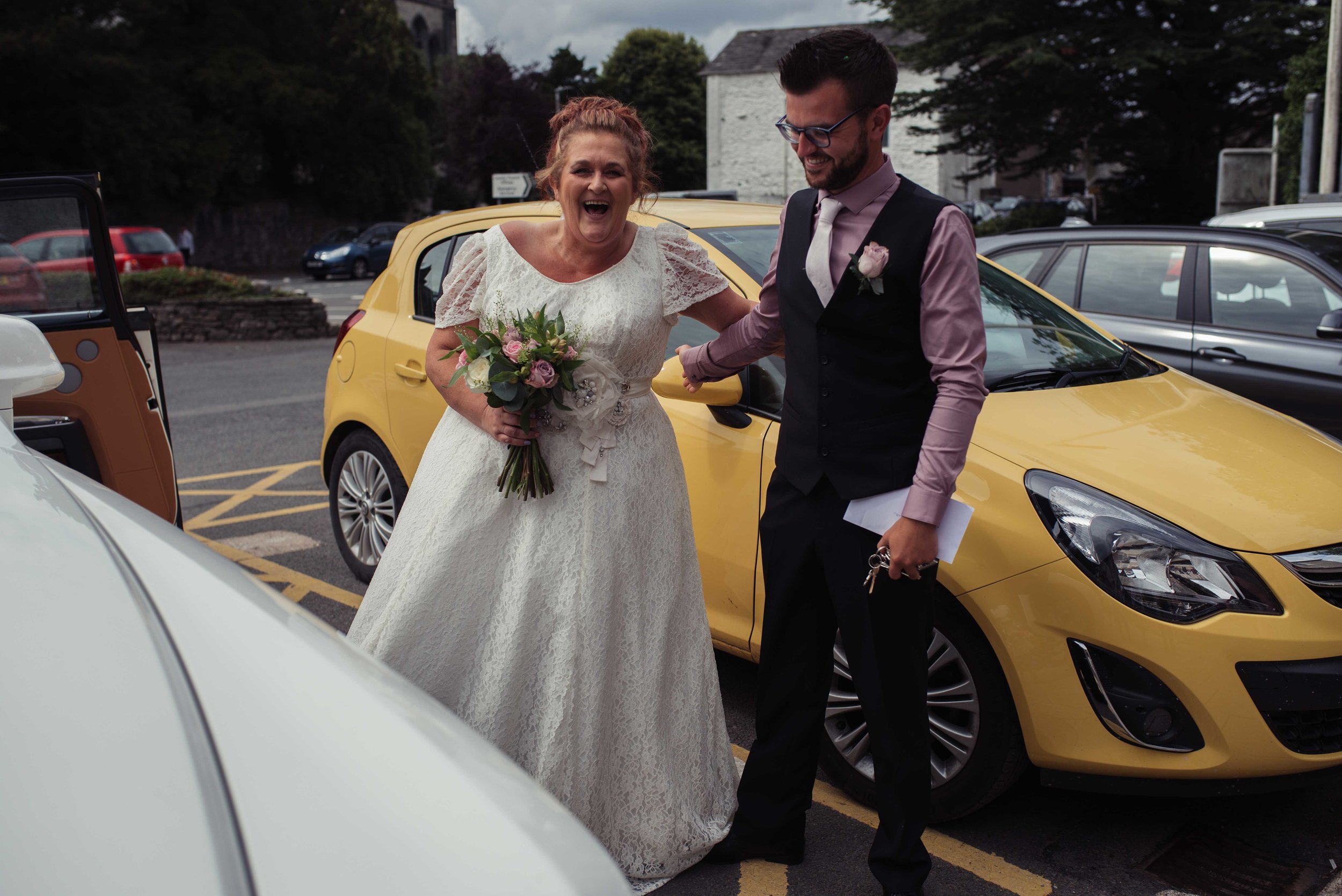 The bride and the best man have a laugh outside the wedding car