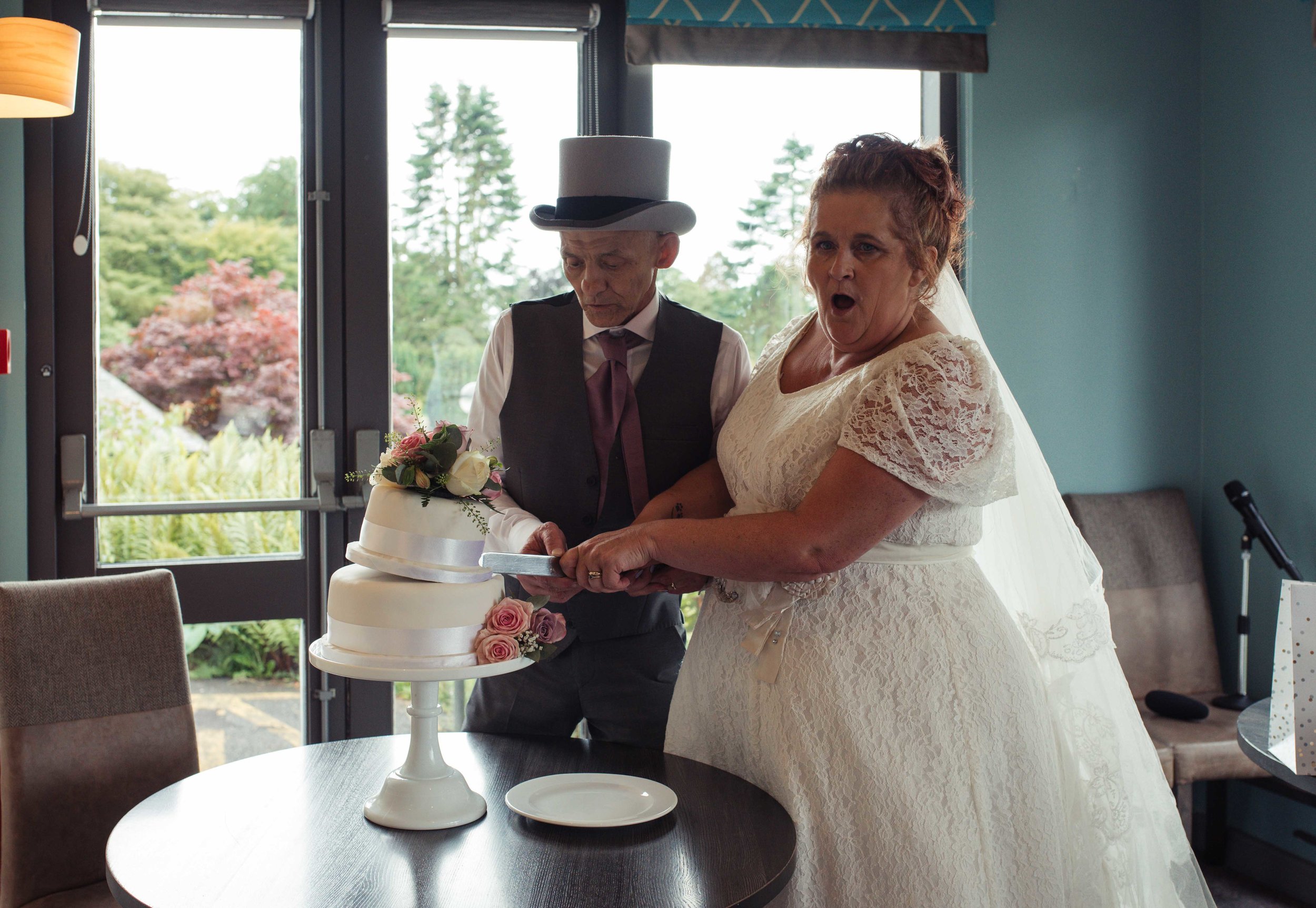 The bride and groom almost make the cake topple as they cut it in the greenhouse restaurant