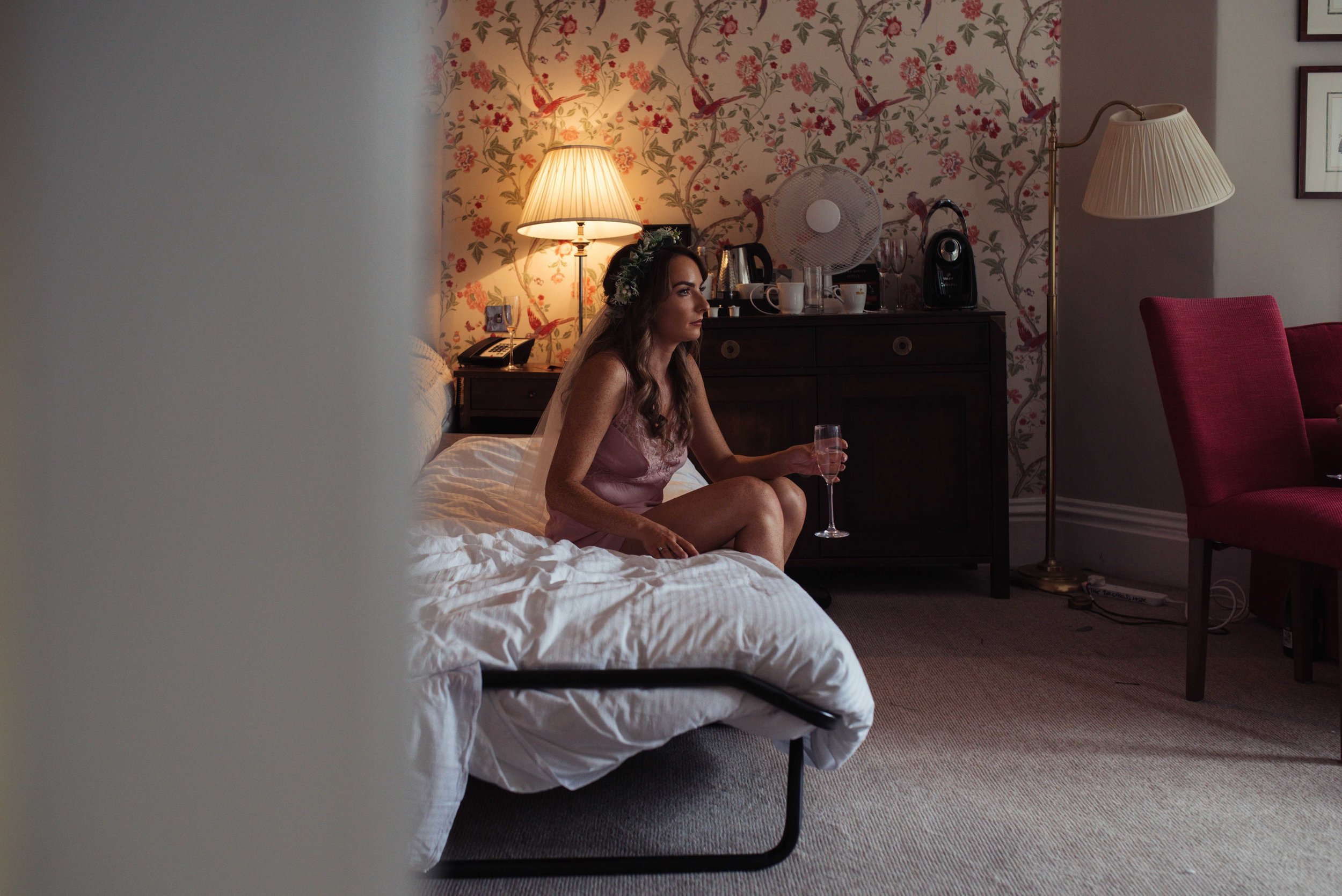 The bride sits on the bed and looks out of the window before her wedding