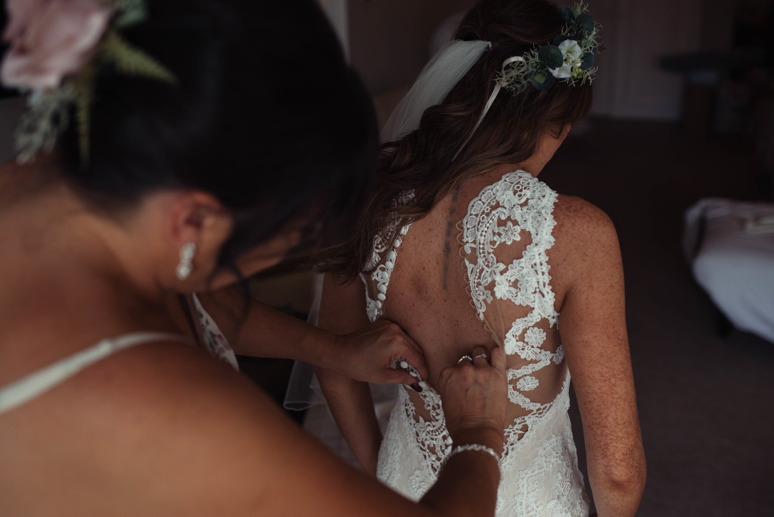 The brides sister helps her into her wedding dress