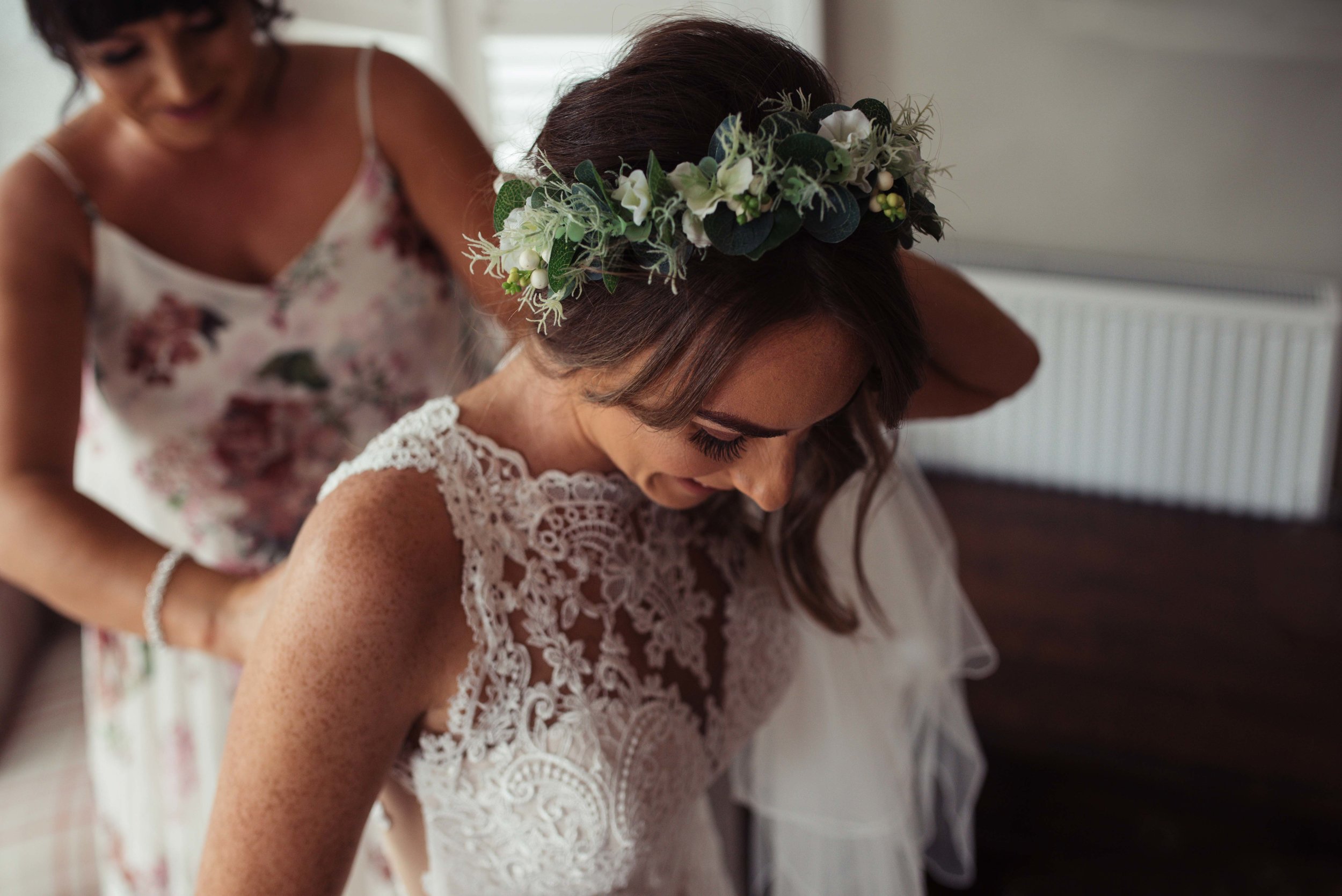 The bride smiles as her sister helps her into her lace wedding dress