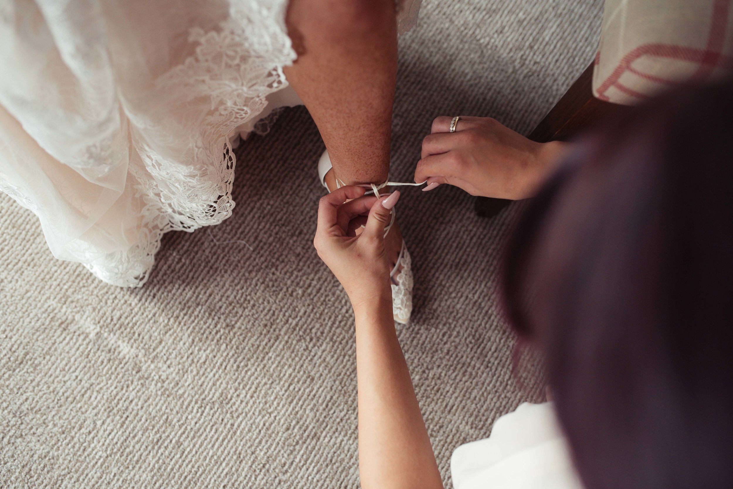 The brides sister helps her put on her lace wedding shoes