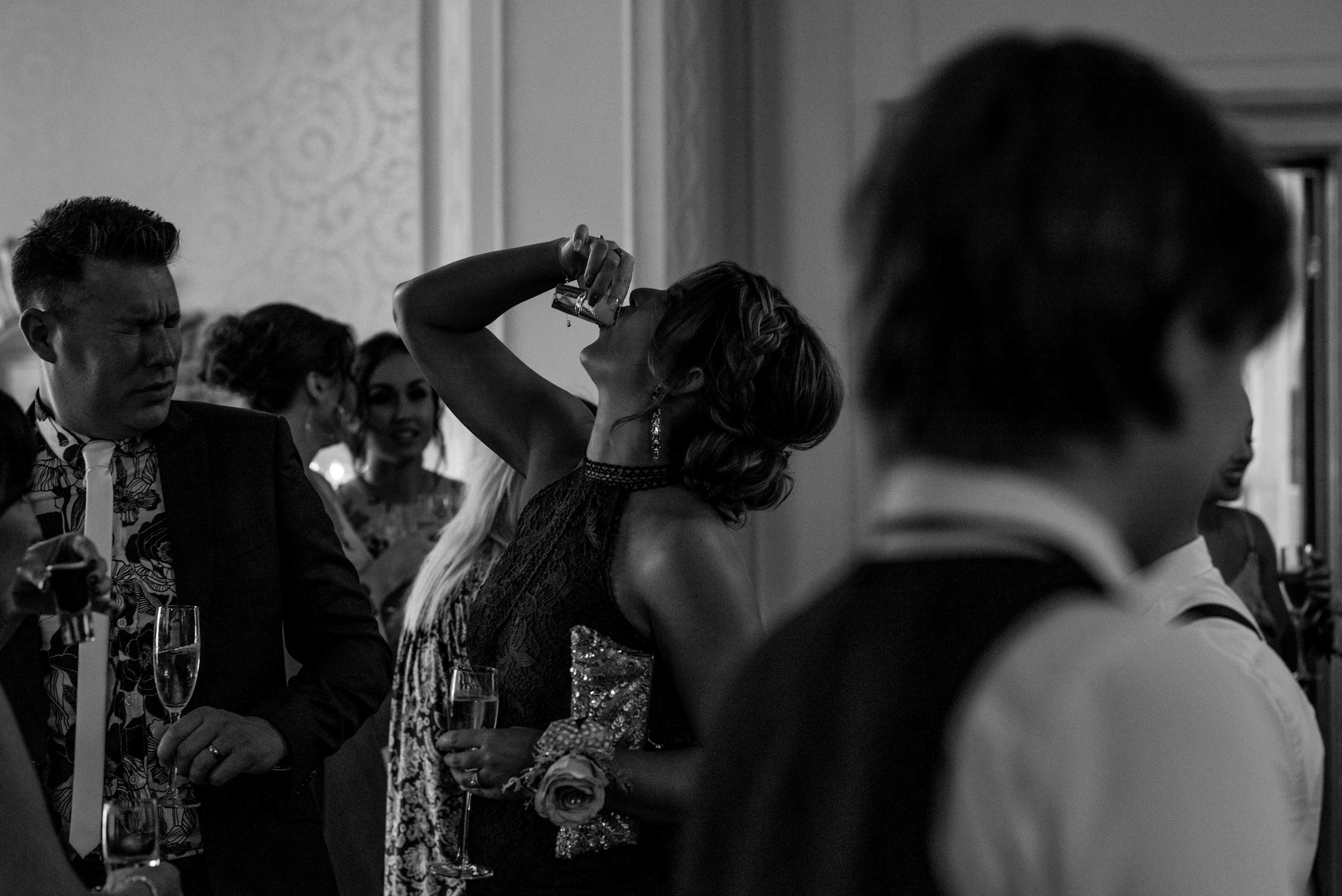 A wedding guest puts her head back to swallow a vodka shot
