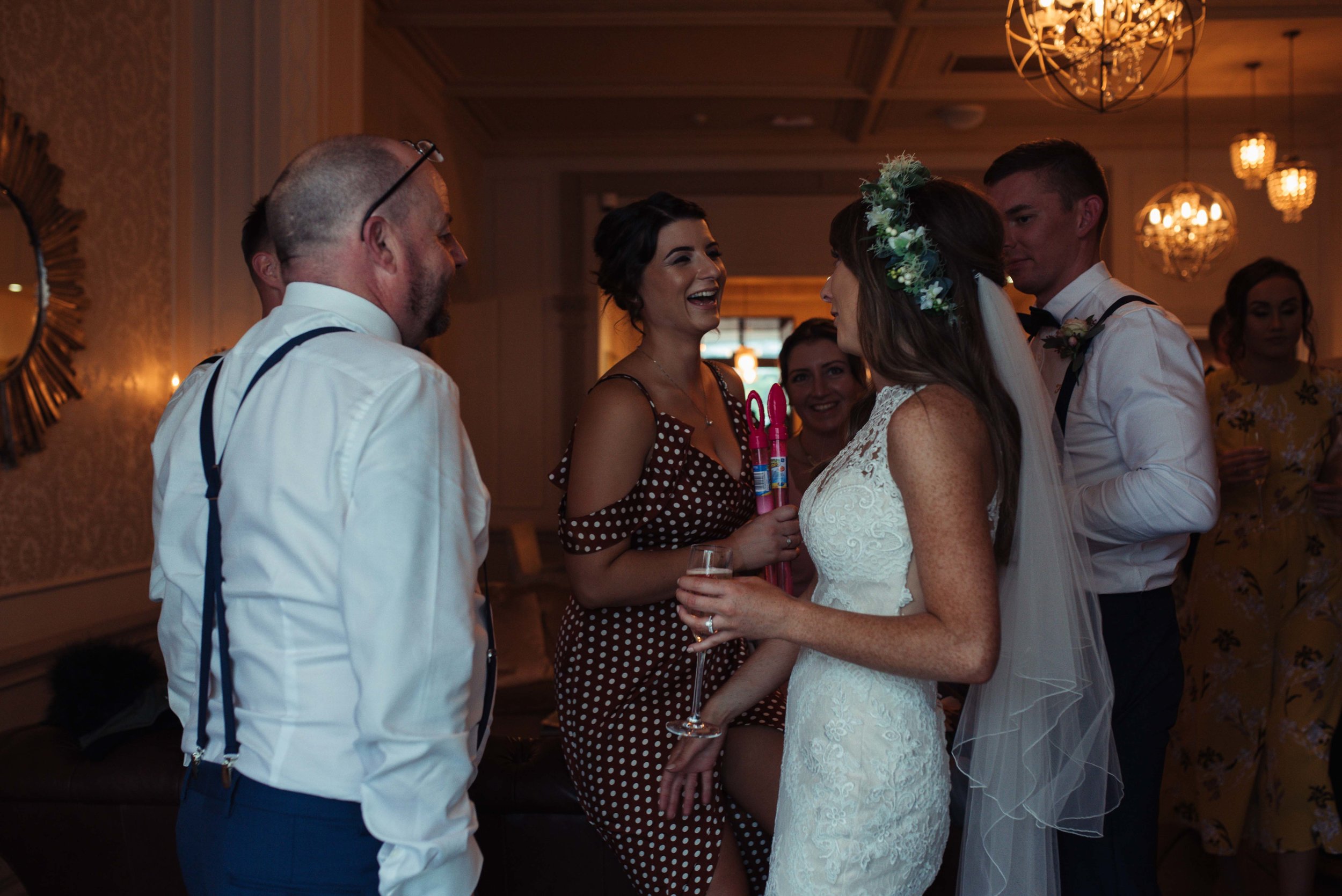 The bride stands and talks to friends in the bar at The Belsfield