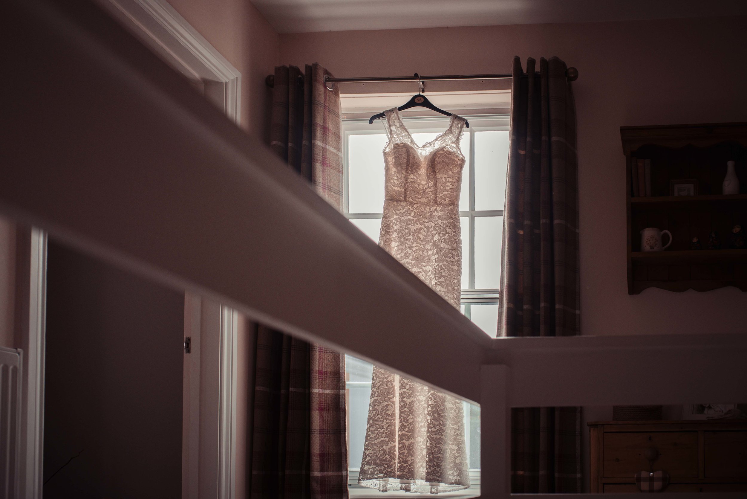 The brides dress hanging in the hallway in front of the window