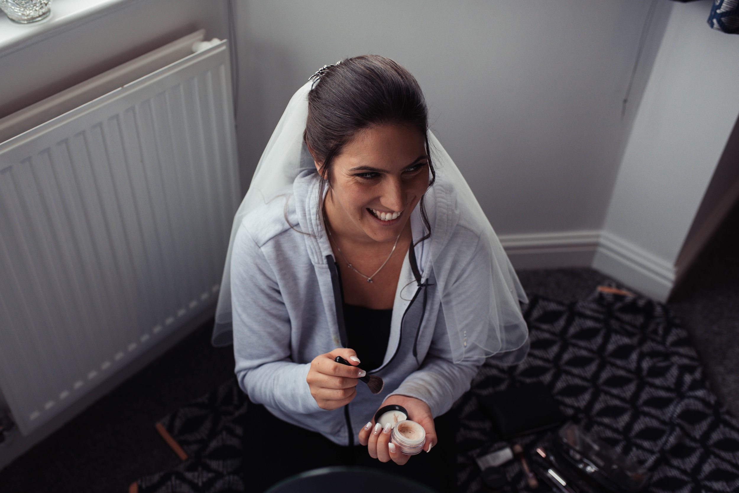 The bride sits on the floor and does her own makeup