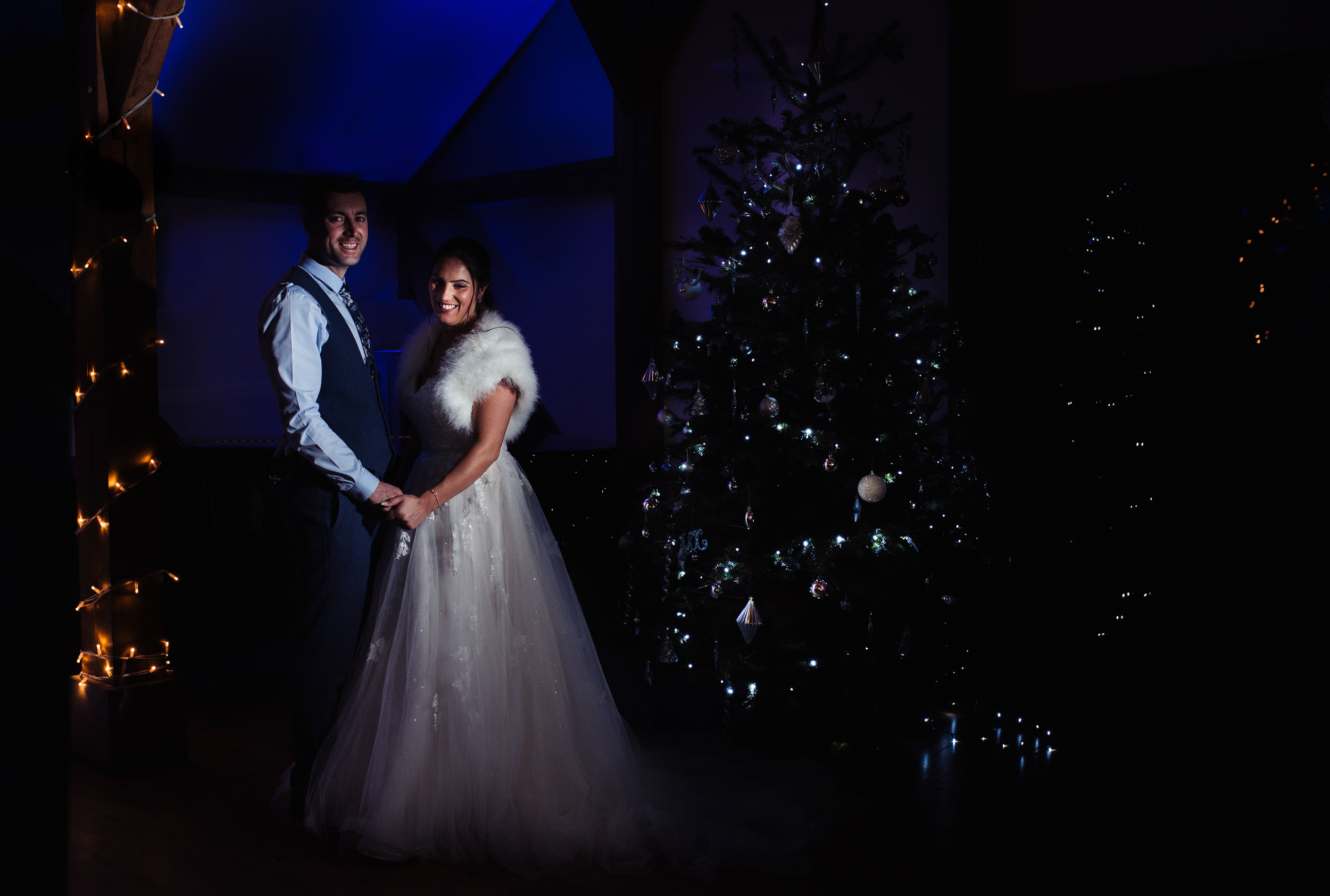 The bride and groom pose in front of the Christmas tree at Sandhole Oak Barn