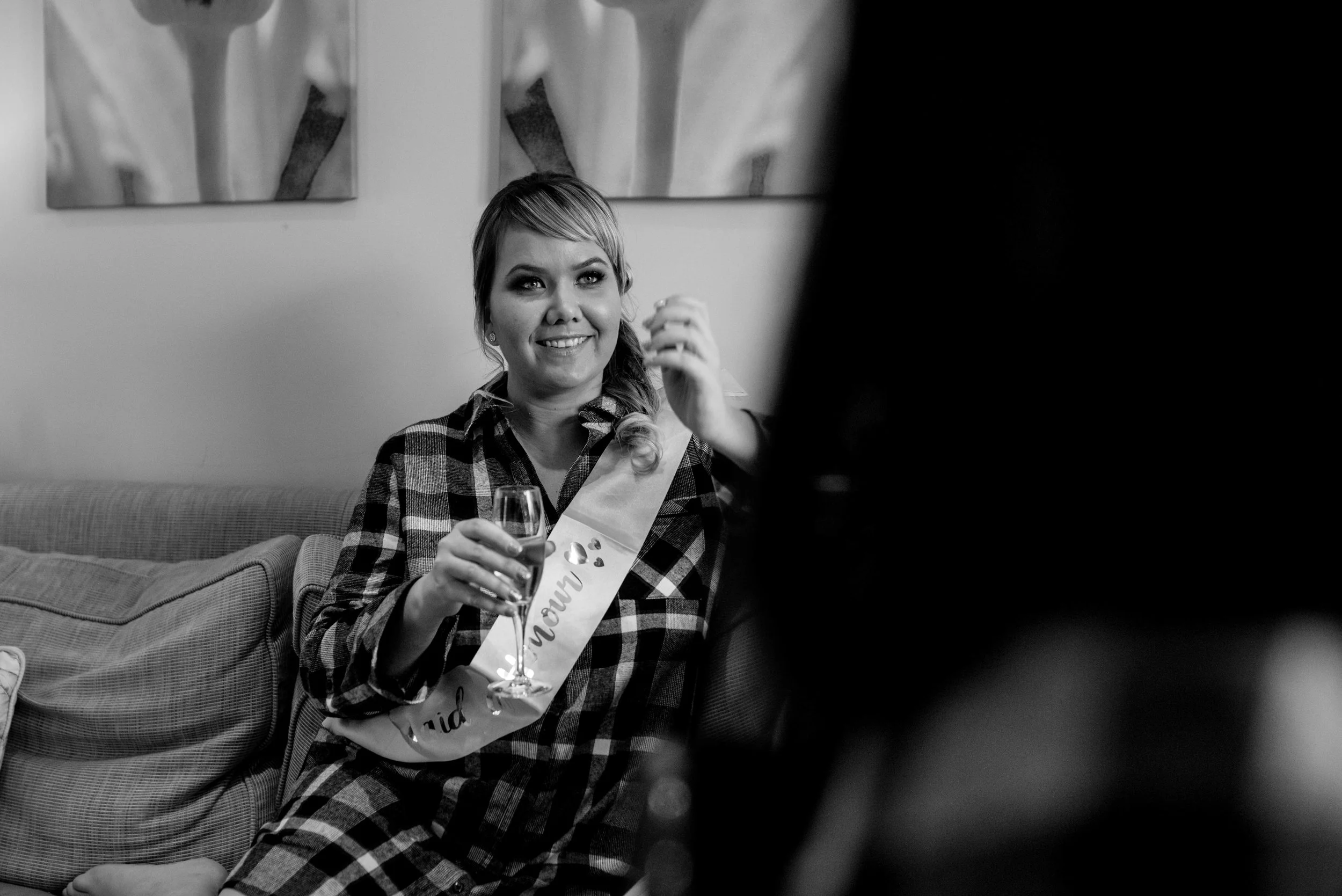 Sister of the bride sits on the sofa wearing a sash from the hen do