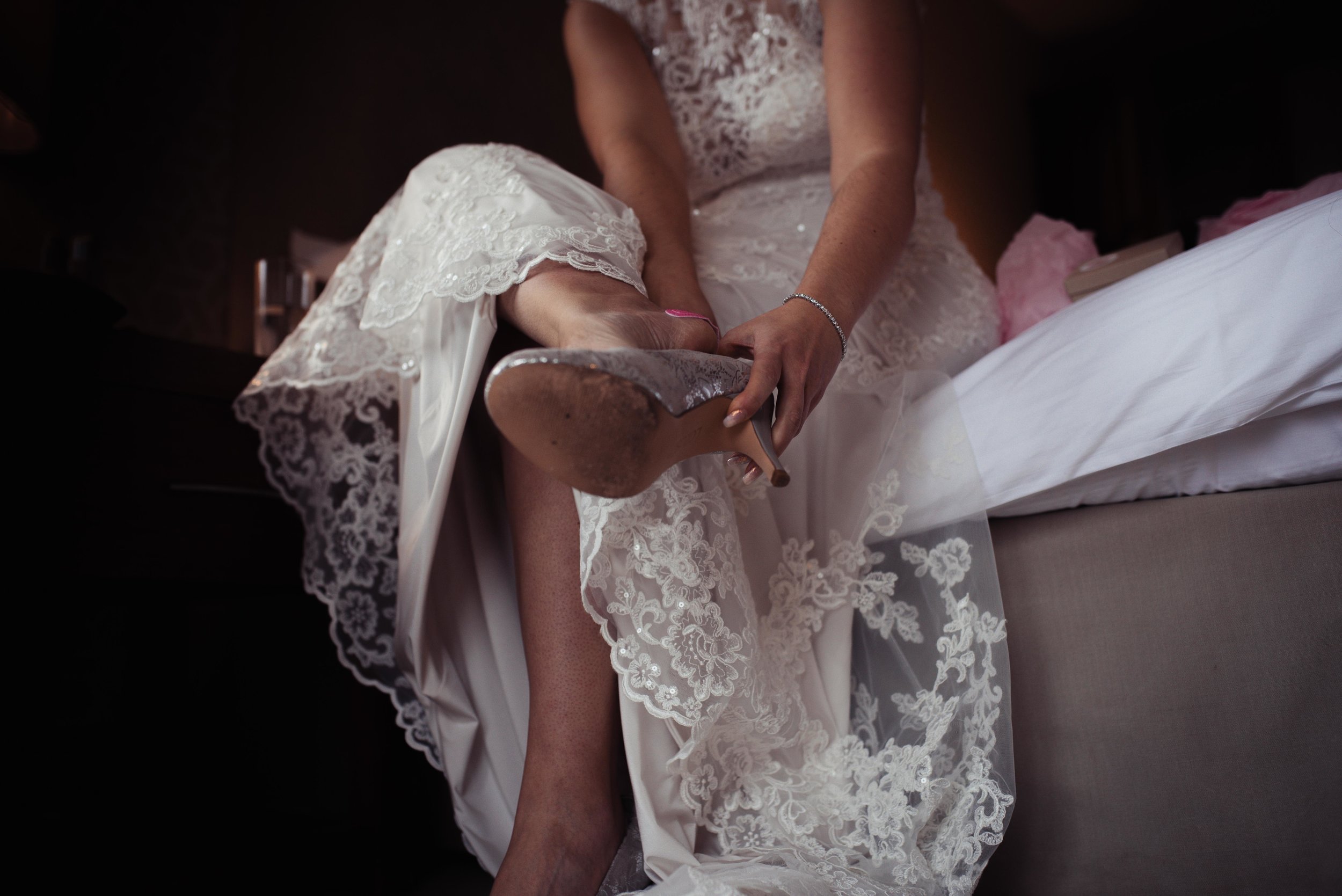 The bride sits on the side of the bed to put her wedding shoes on