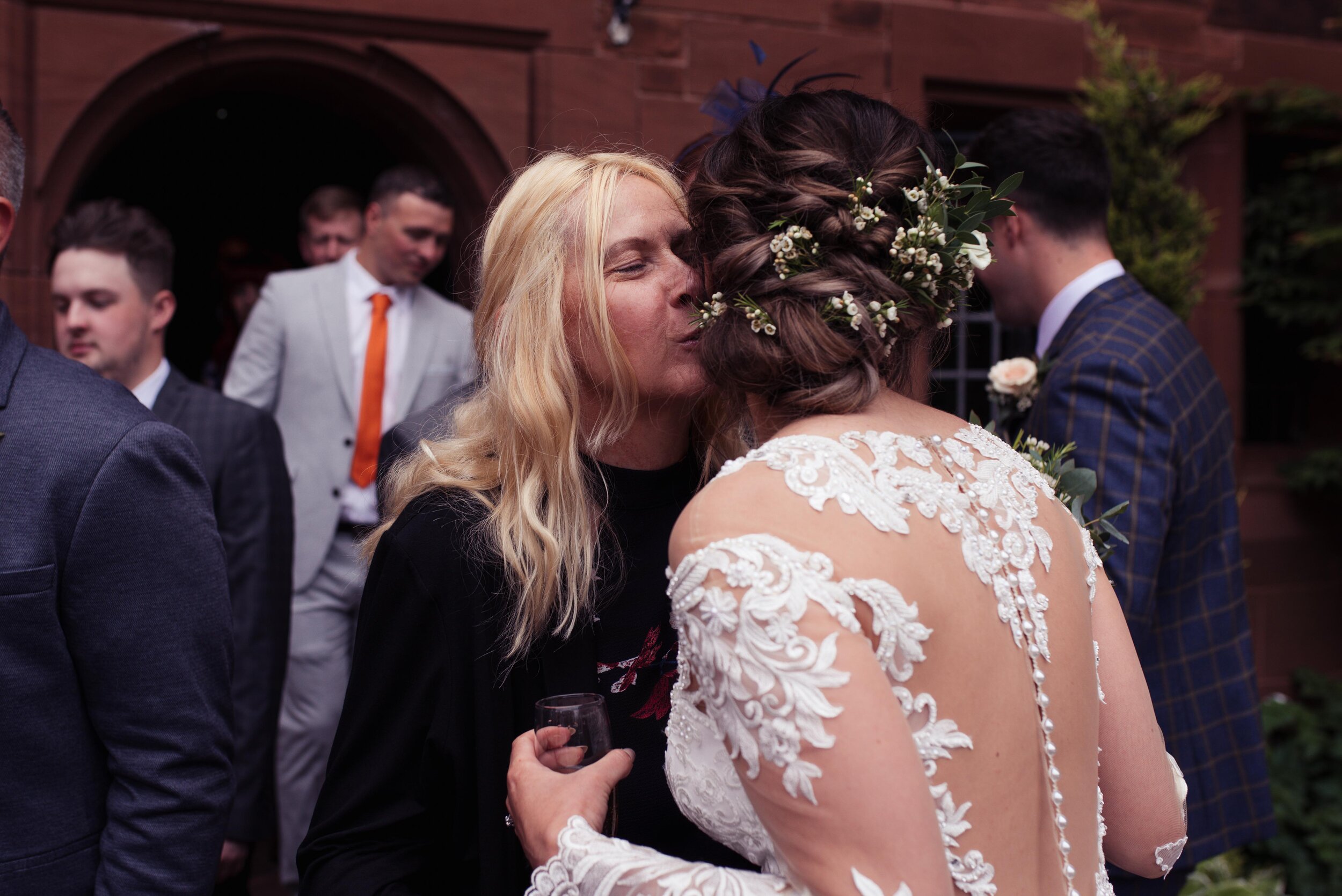 A blonde wedding guest gives the bride a kiss on the cheek