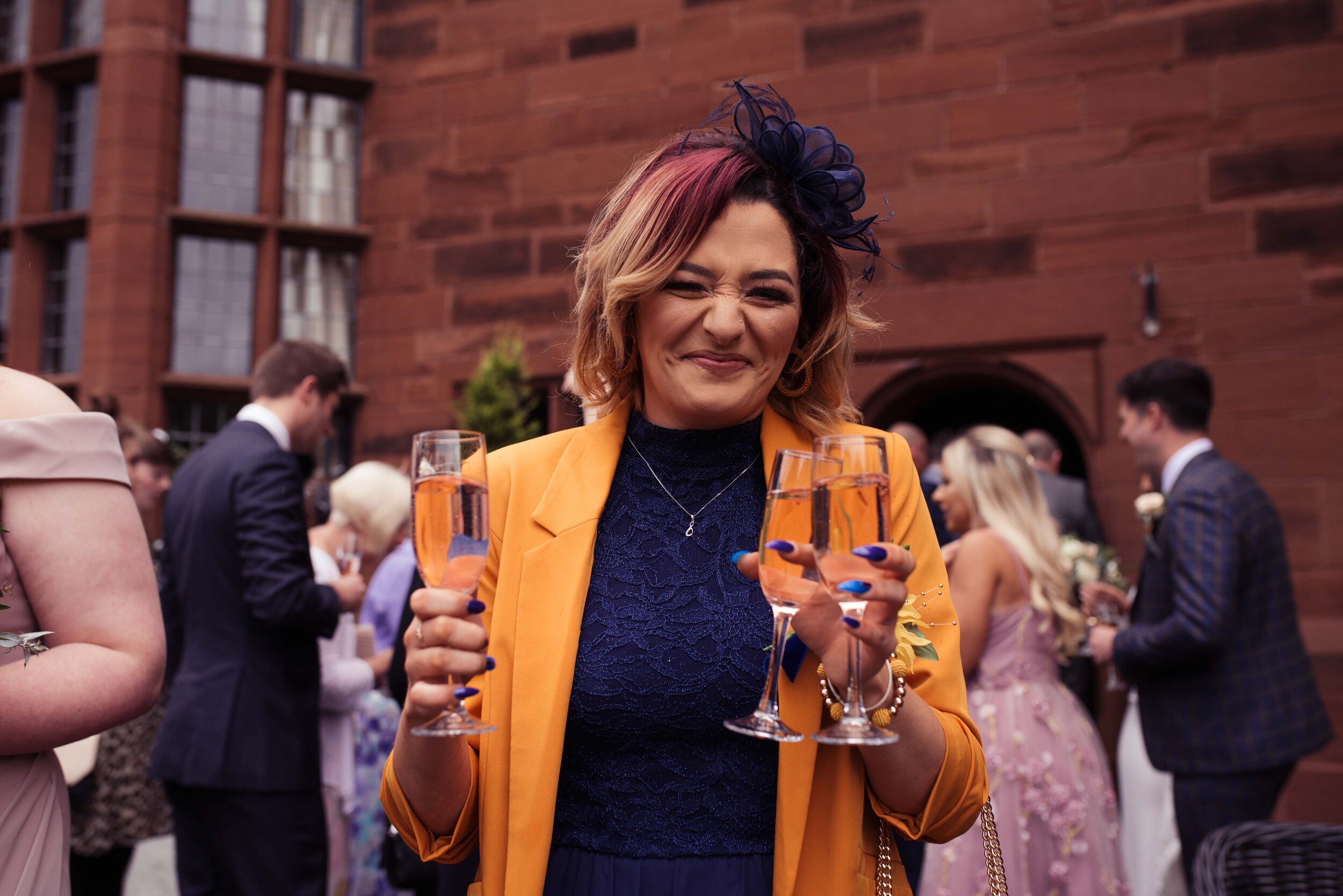 Wedding guest in a yellow jacket carrying two glasses of prosecco