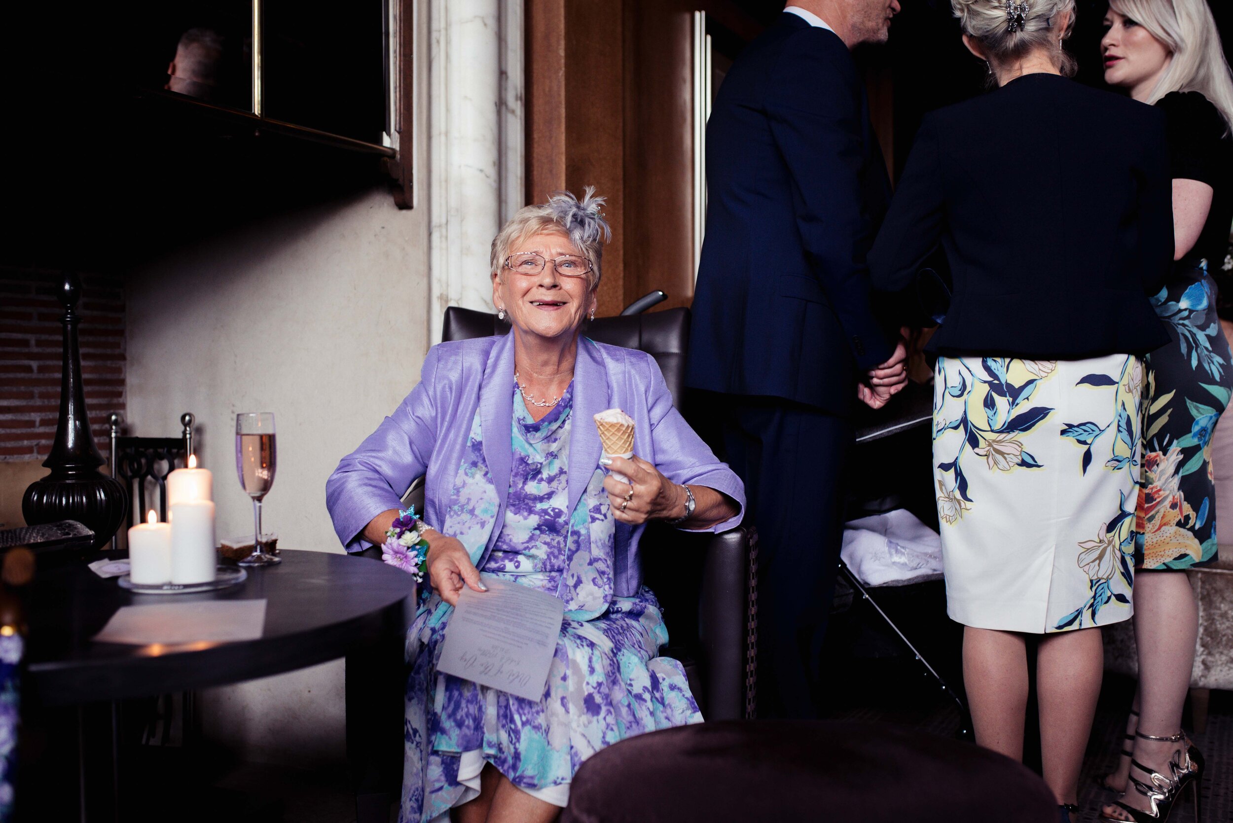 An elderly wedding guest sits in the bar eating an ice cream