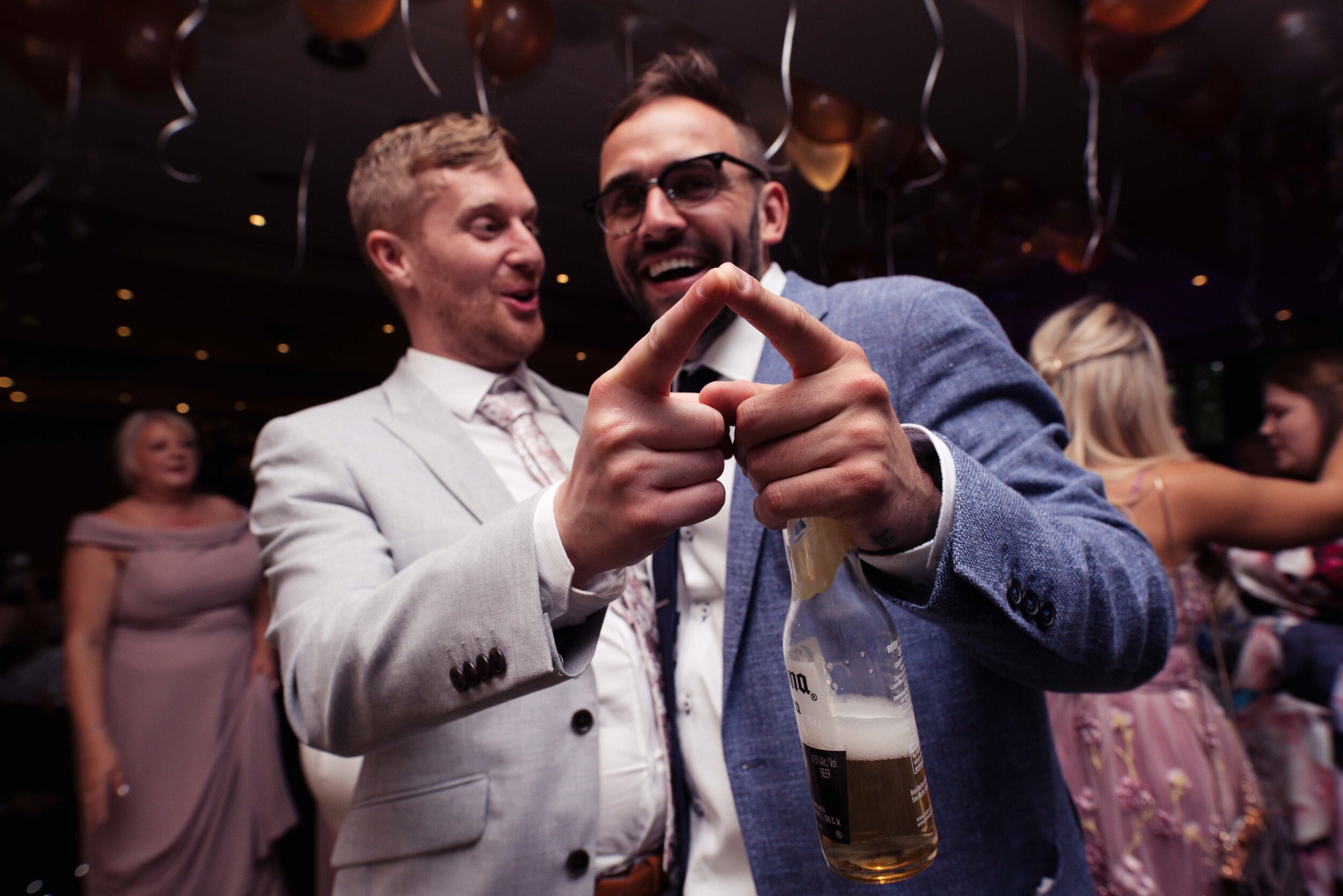 Two male wedding guests pointing towards the camera on the dance floor