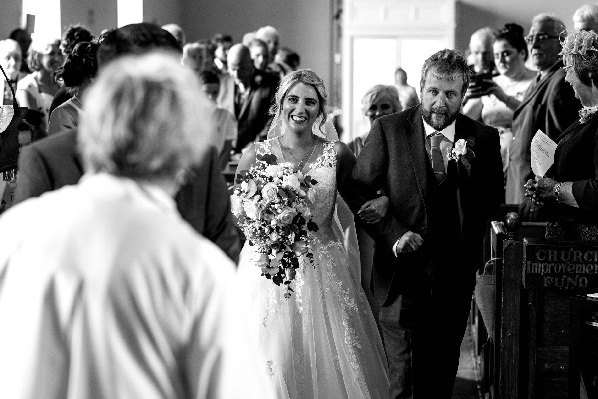 A very smily bride enters the church with her brother on her arm